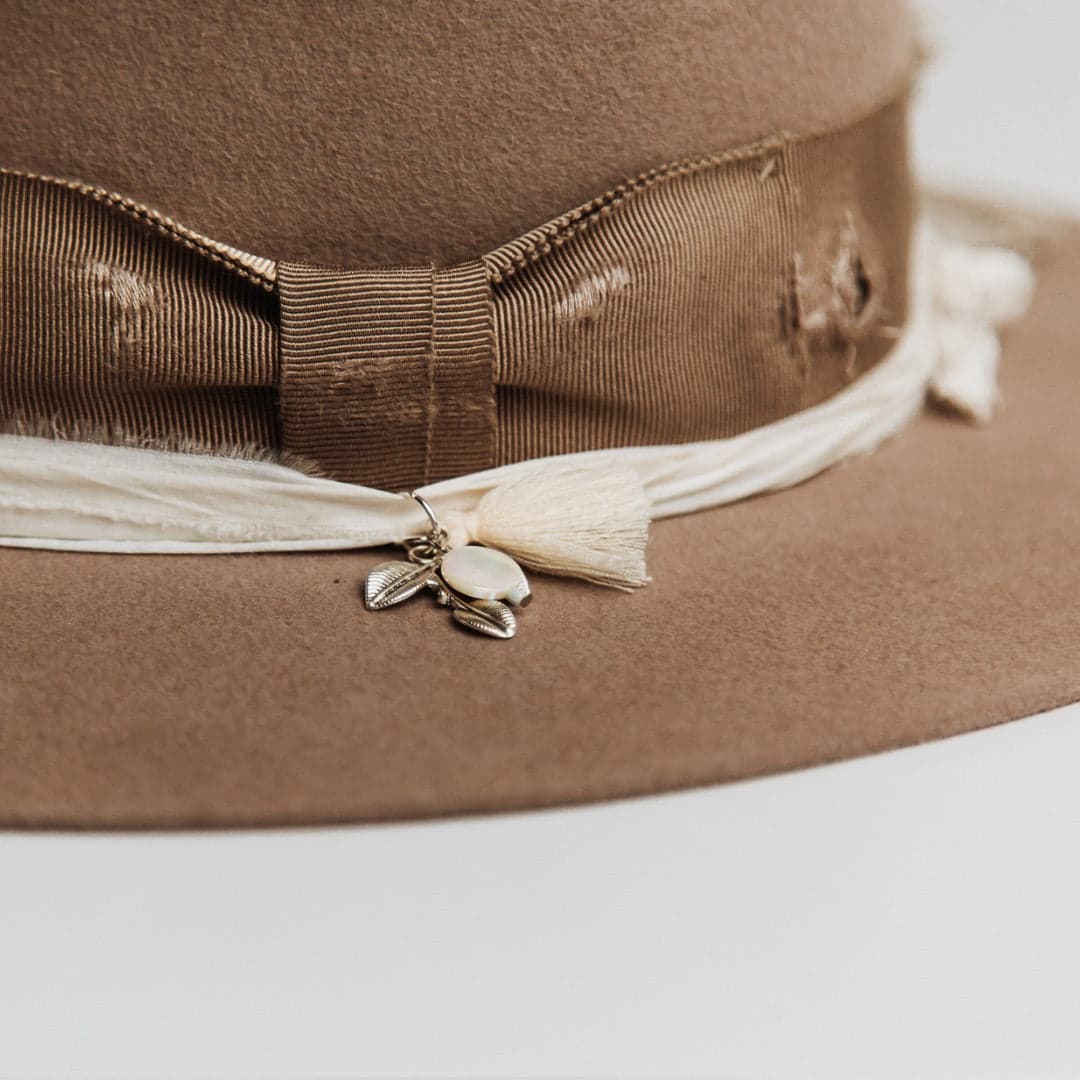 Close up detail of the Enso felt hat showing charm cluster with ivory tassel, silver charm and moonstone.