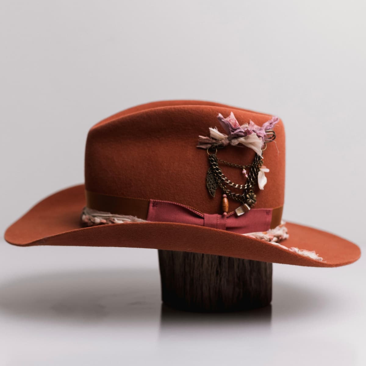 Left side view of the Spiced Pumpkin felt cowboy hat Evans by PHYLLi Designs with bronze chunky hat pin featuring tassel, sari silks and charms.