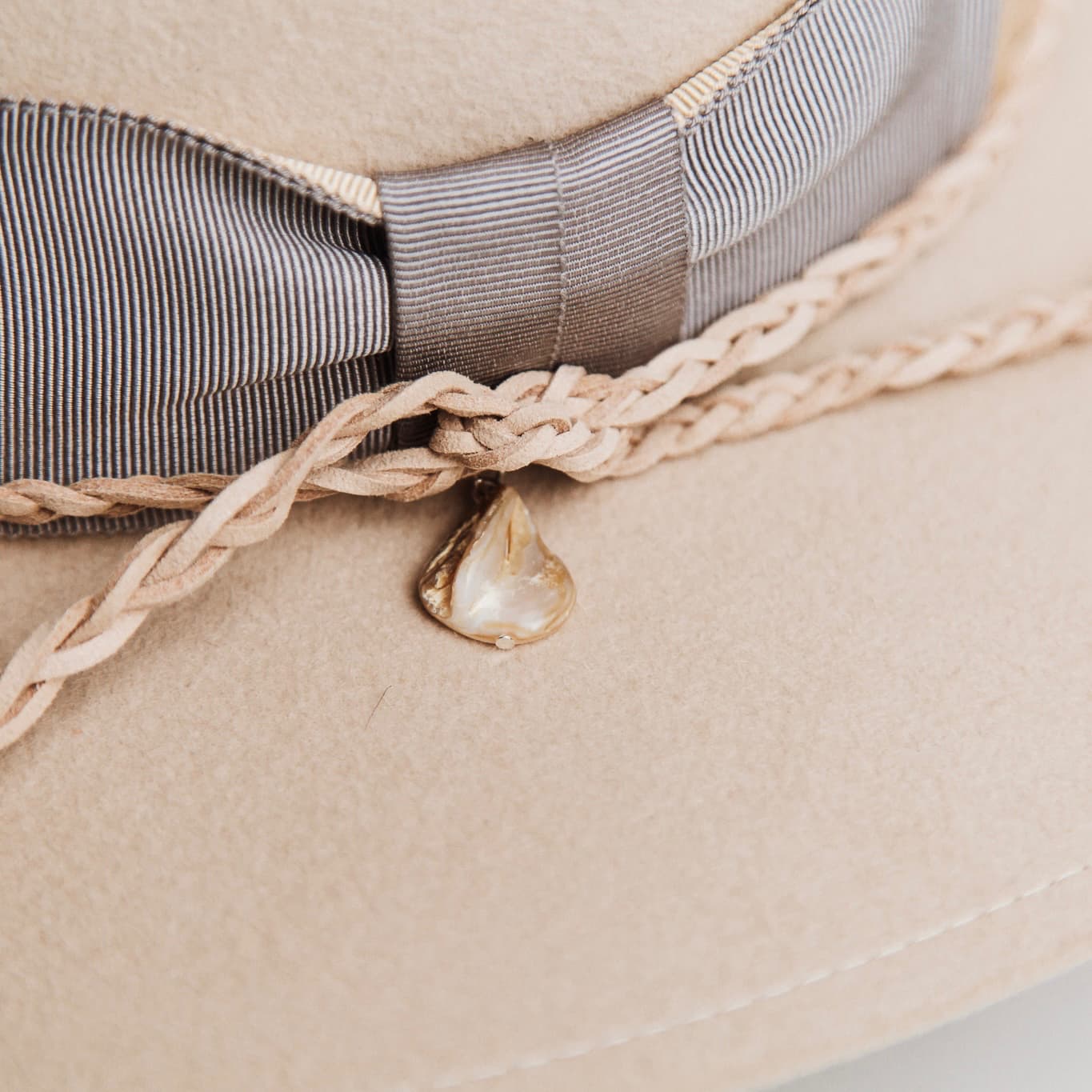 Close-up detail of Fallon beige felt hat trim by PHYLLi Designs showing ivory brim stitch, grosgrain trim and pearl pendant detail.
