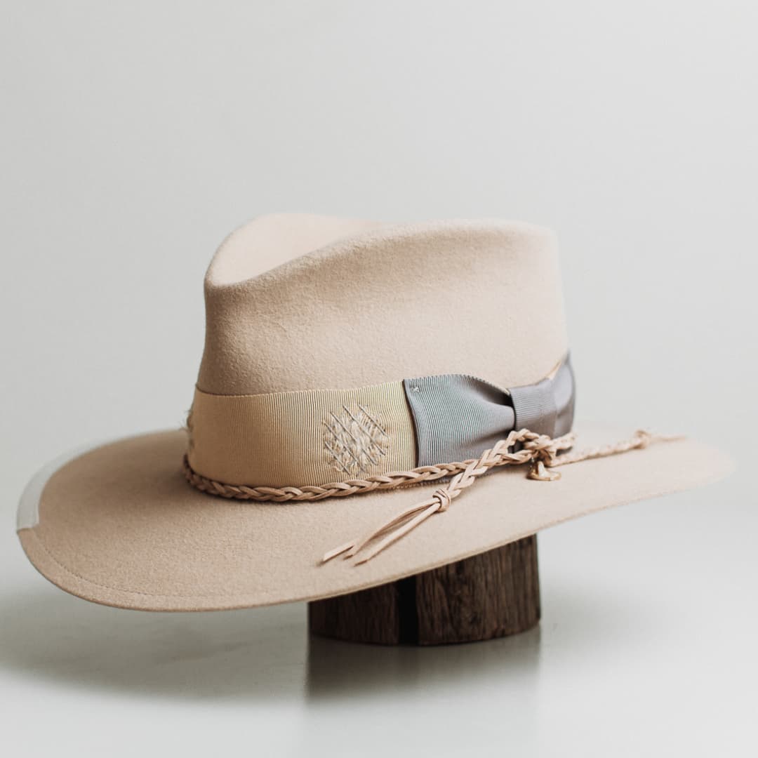 Front left angle of Fallon beige rabbit felt hat by PHYLLi Designs showing distressed grosgrain band, dove darning patches and pearl pendant trim.