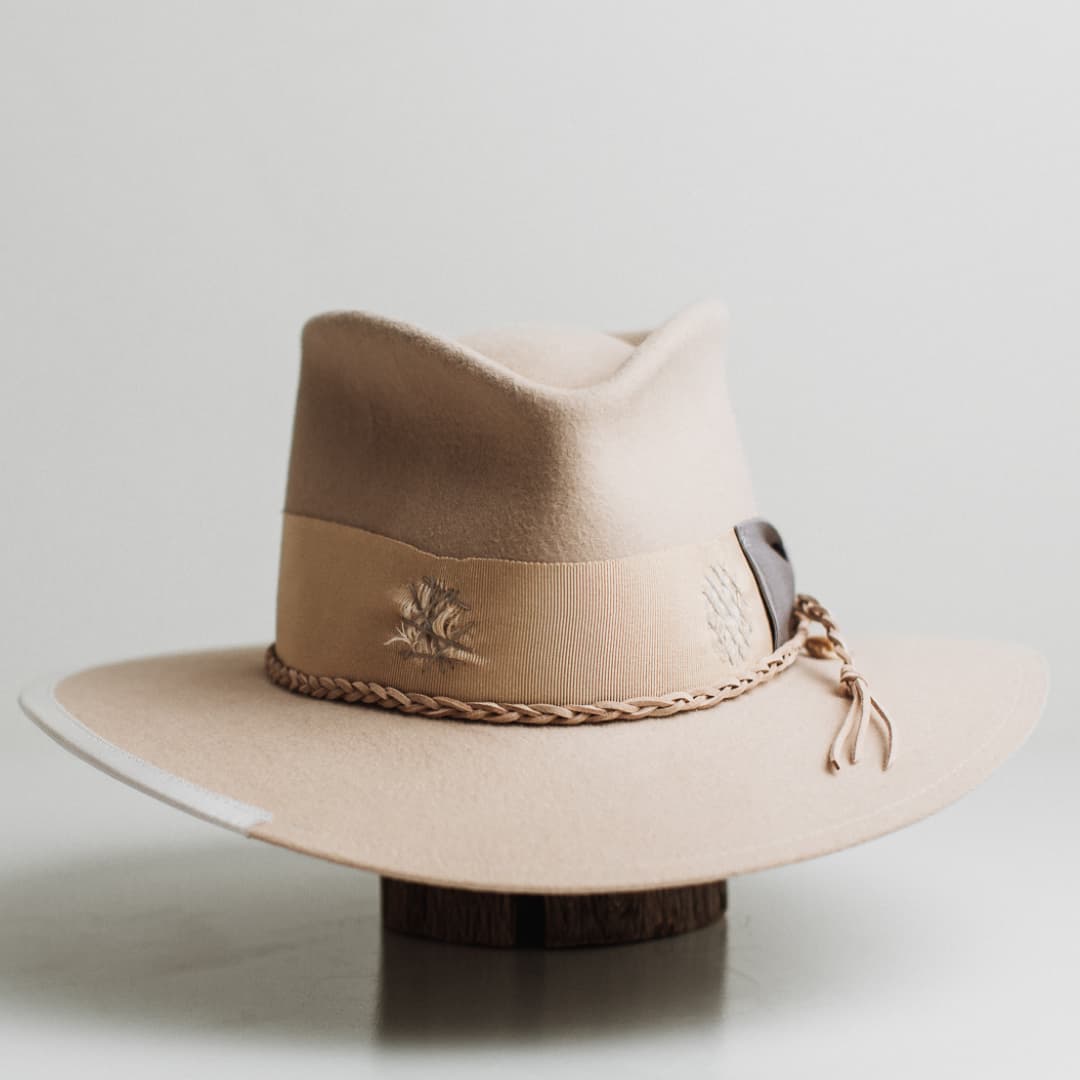 Front view of Fallon beige premium felt hat by PHYLLi Designs with distressed sand grosgrain band, dove bow and pearl pendant on white background.