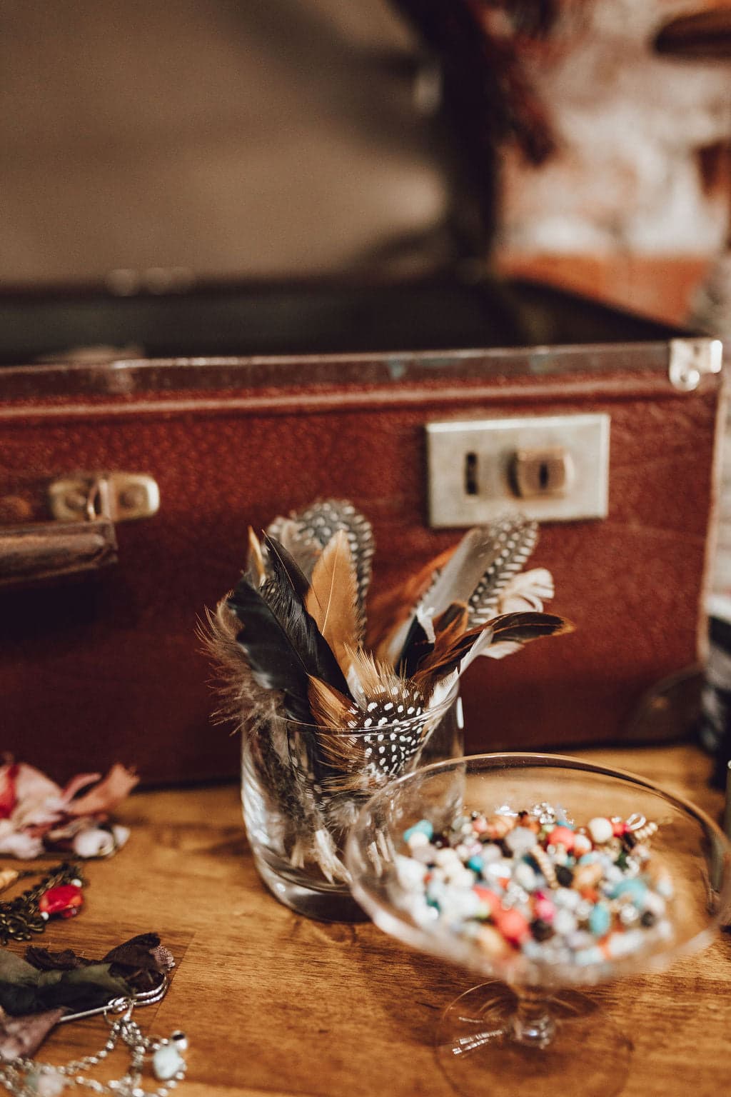 Close up detail of fallen feather bunches displayed beside a vintage case and jewellery trims in a hatmaking studio setting.