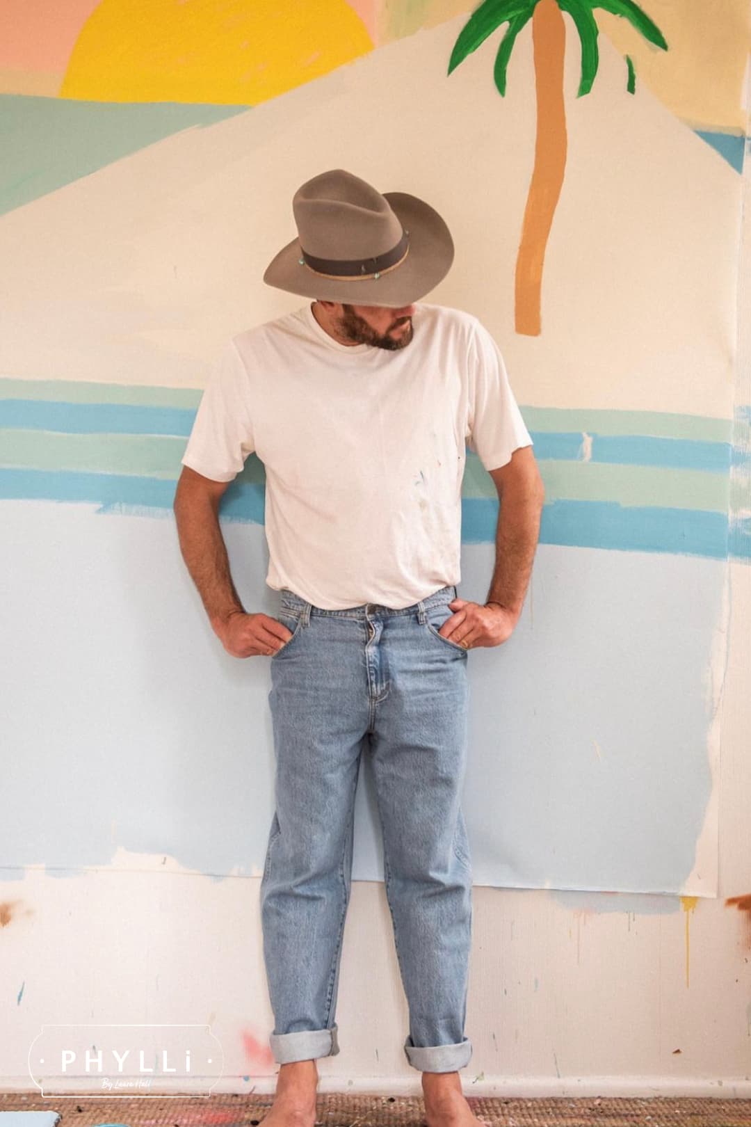 Artist Jacob Pedrana wearing the Finse cement felt cowboy hat by PHYLLi Designs with distressed steel grey grosgrain band in an artist studio with painted wall backdrop.