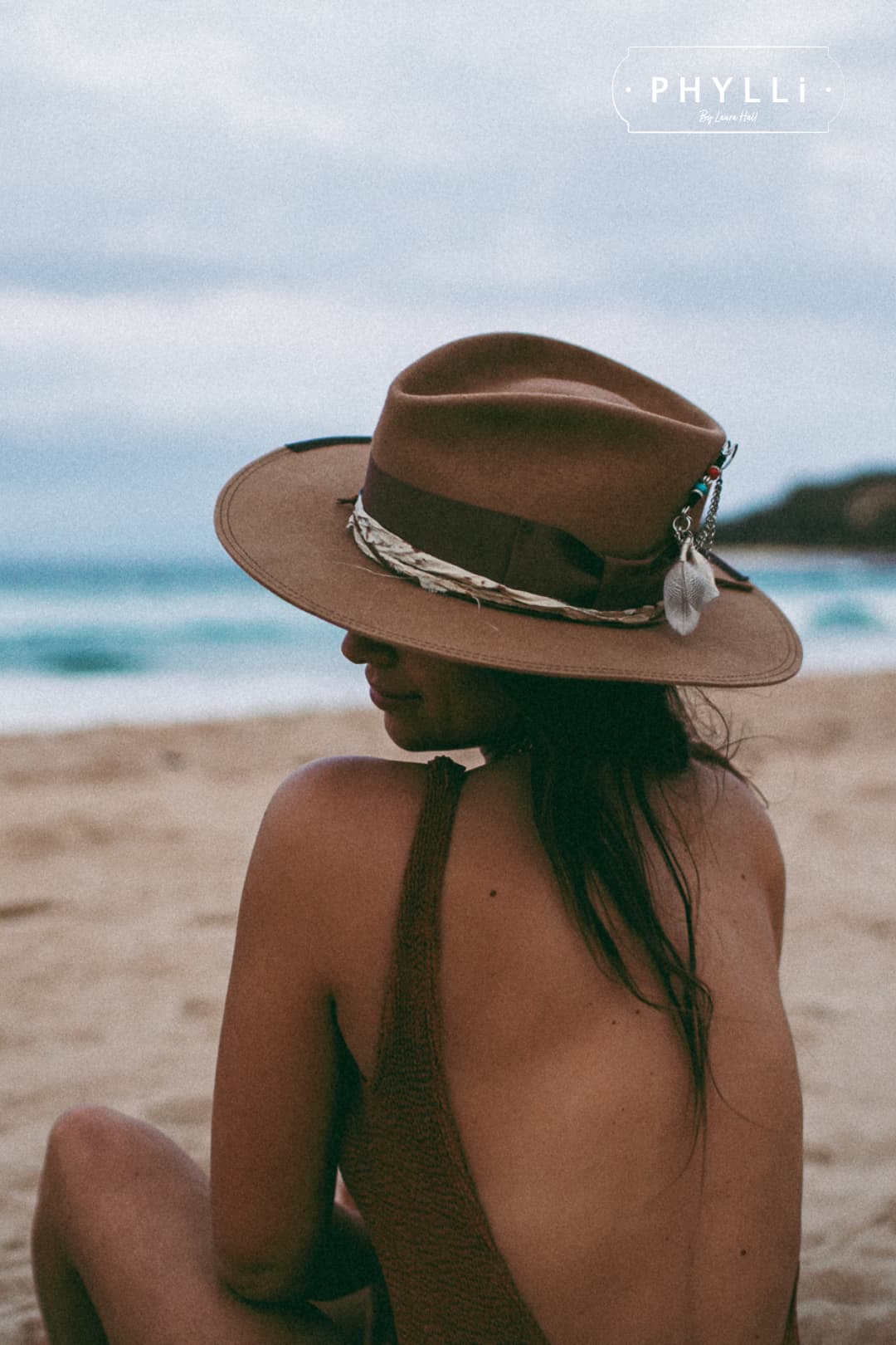 Side profile of woman wearing Fly Fisher camel felt hat by PHYLLi Designs on the beach showing sari silk trim and silver chunky hat pin.