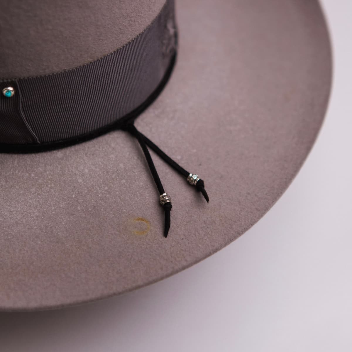 Close up detail of the Franco felt hat showing black suede string finished with silver hardware tips.