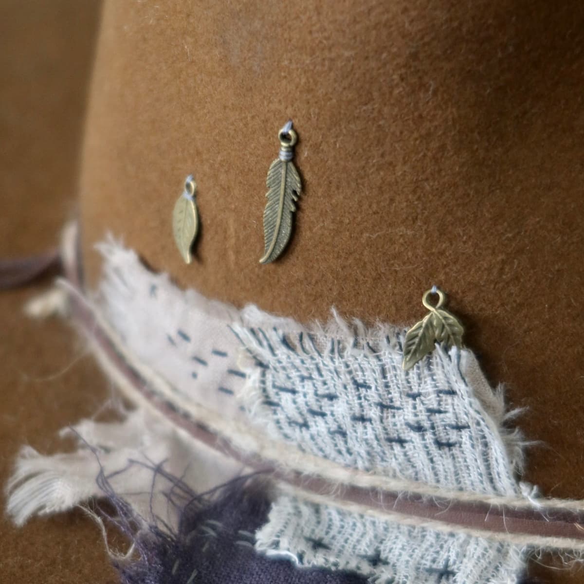 Close up detail of the George Limited Edition felt hat showing antique bronze feather and leaf charm cluster.