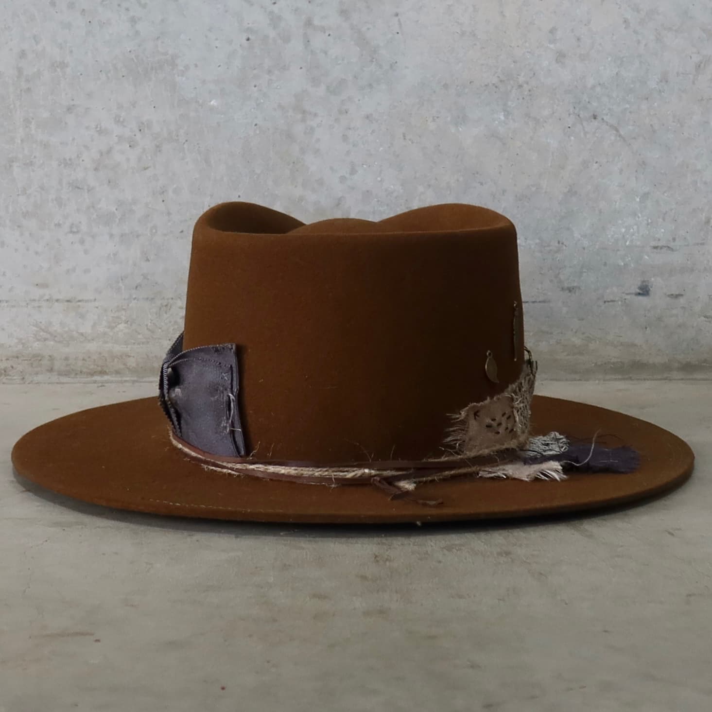 Back view of the caramel felt hat George Limited Edition by PHYLLi Designs featuring Wabi Sabi linen patches, bronze feather and leaf charms, and partial double brim stitch.