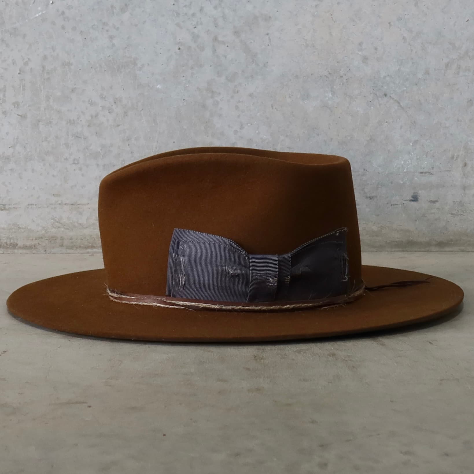 Left side view of the caramel felt hat George Limited Edition by PHYLLi Designs with floating steel grosgrain bow and twine wraps.