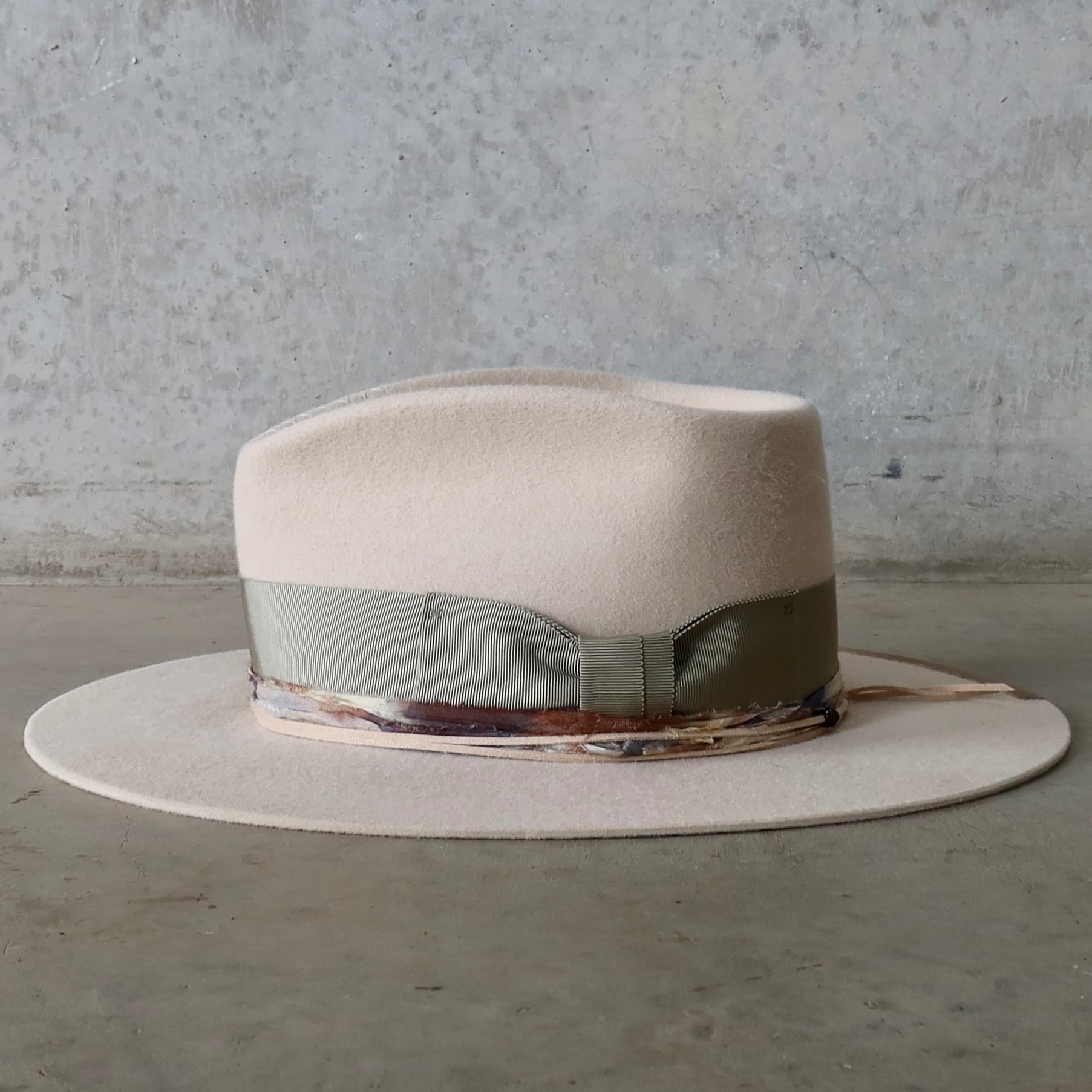 Left side view of the beige felt hat Grasslands by PHYLLi Designs with sari silk trim and nude suede string with wooden beading.