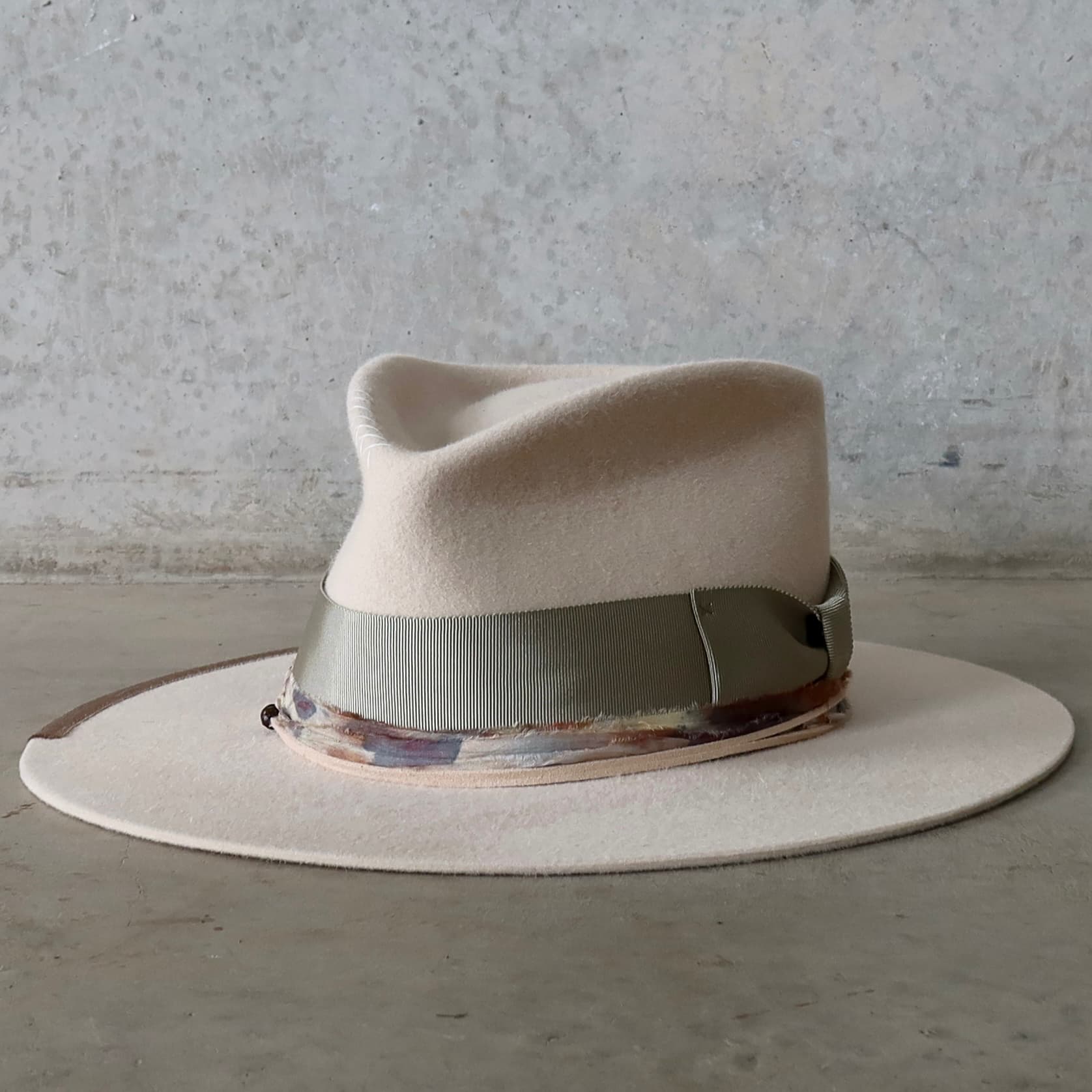Front left angle of the beige felt hat Grasslands by PHYLLi Designs with oil green grosgrain bow band and speckled blue sari silk trimming.