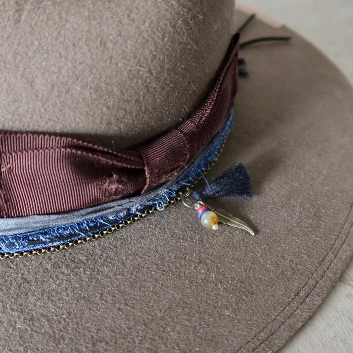 Close up detail of the Grove felt hat showing bronze crown chain with bead charm, bronze feather and black tassel.