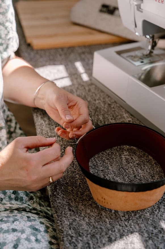 Close up detail of hand stitching a leather hat sweatband beside a sewing machine during the hat resizing process in a studio.