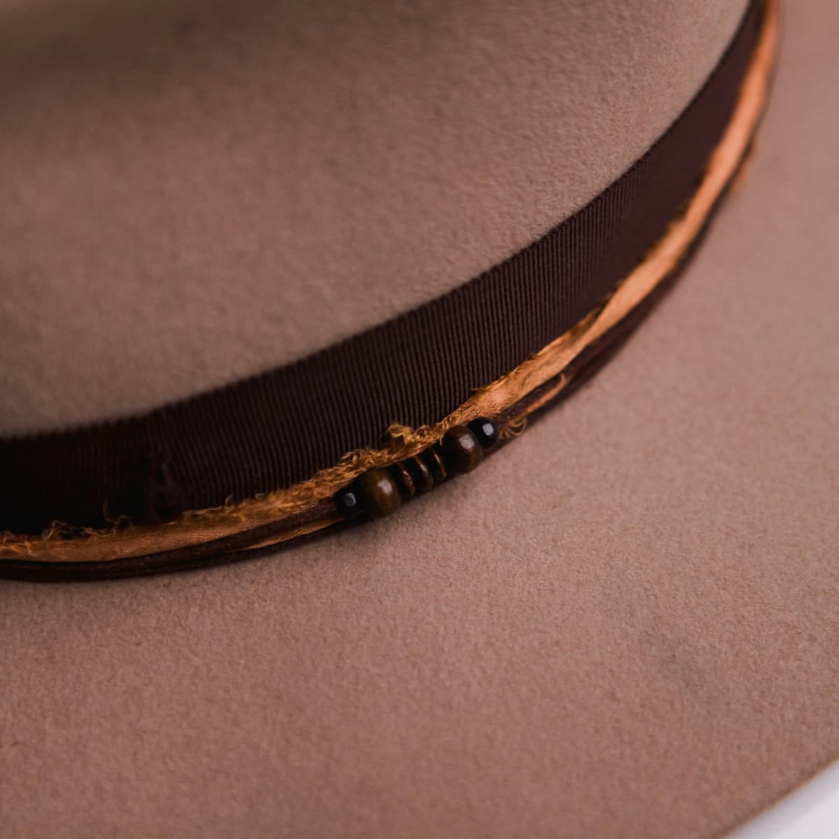 Close up detail of the Hyndman felt hat showing rust sari silk trimming with wooden bead detailing.