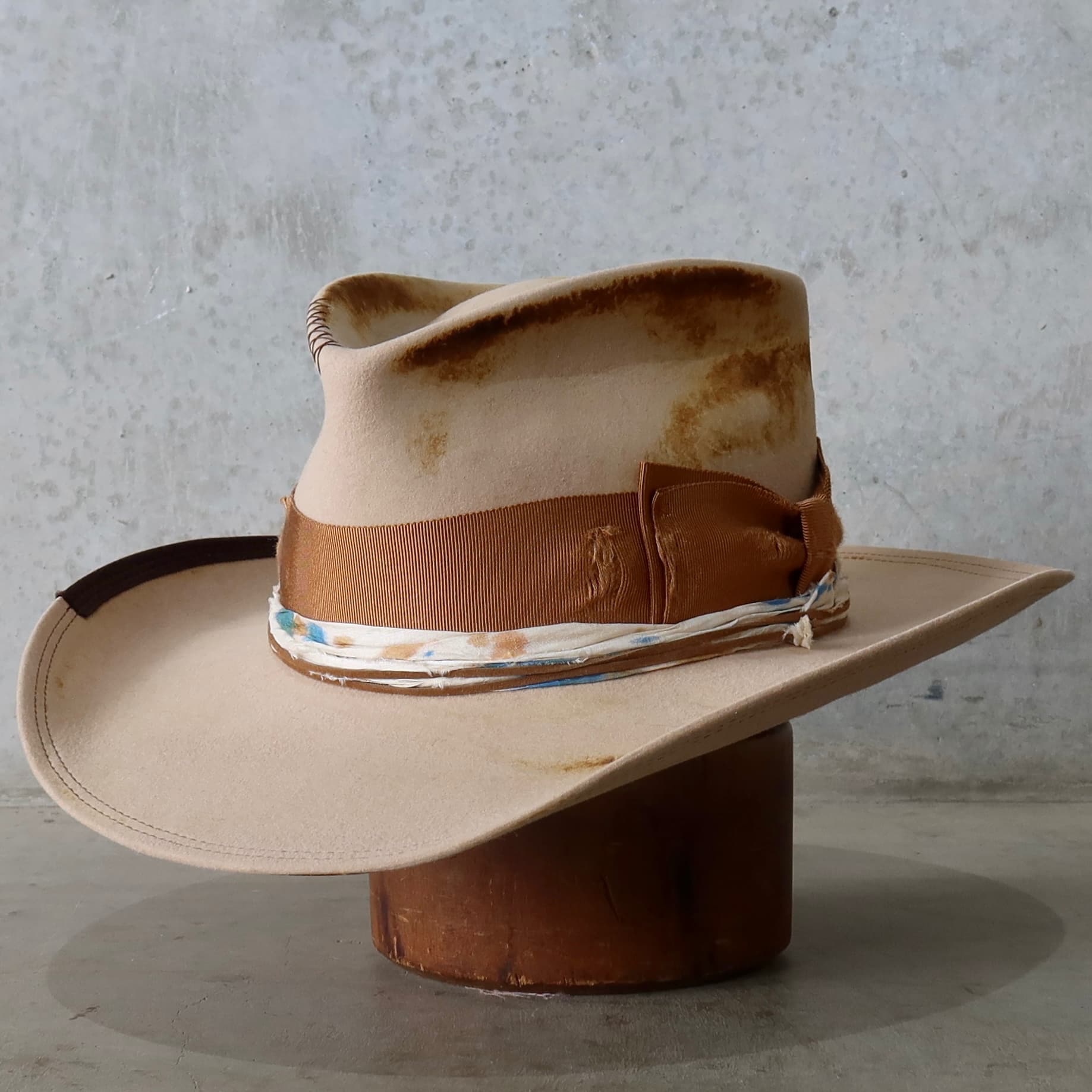 Front left angle of the sand cowboy hat Iluka by PHYLLi Designs with distressed copper grosgrain double bow and dark brown brim stitching.
