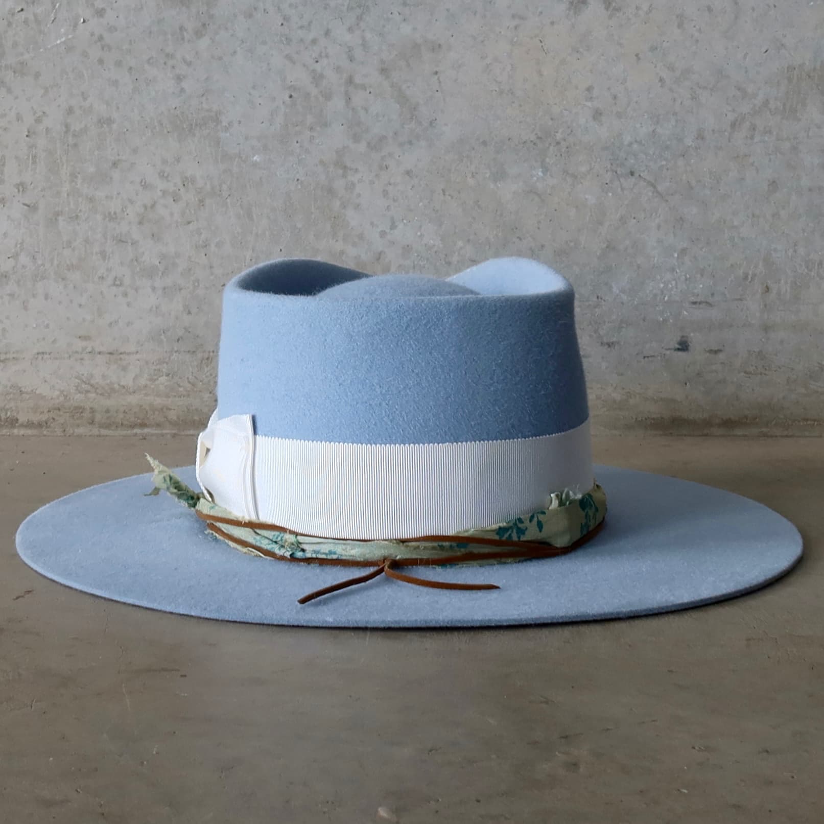 Back view of the crystal blue felt hat Jarvis by PHYLLi Designs featuring blue and teal sari silk trimming and tan suede string tie.