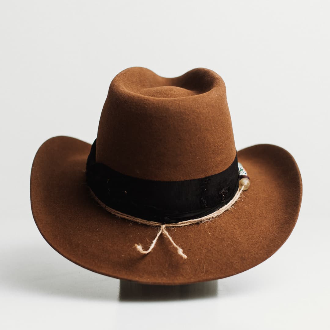 Back view of the Jersey caramel felt cowboy hat by PHYLLi Designs featuring distressed black darned patches and twine wraps with Ghana glass beads.
