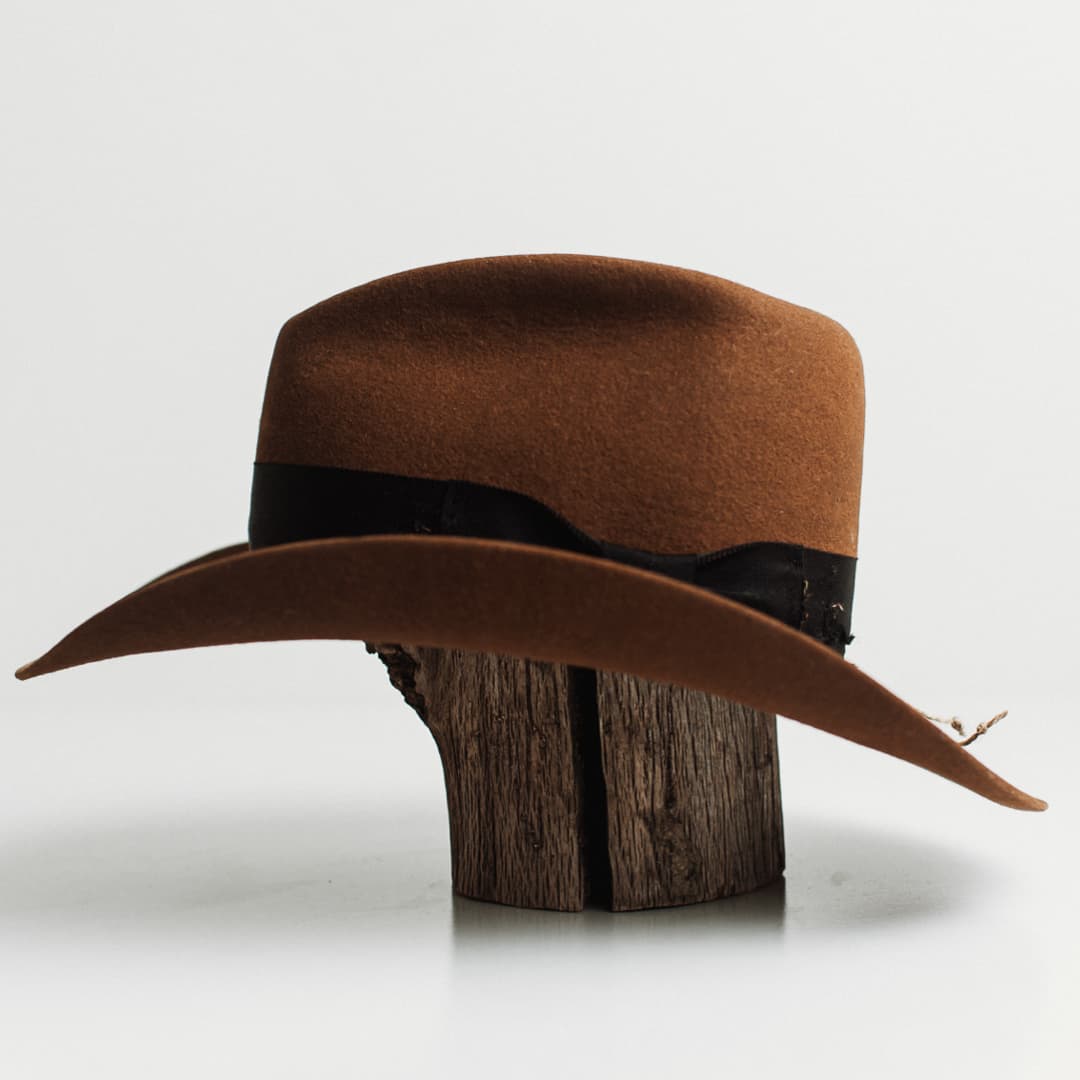 Left side view of the Jersey caramel felt cowboy hat by PHYLLi Designs with distressed black grosgrain band, black darned patch and twine wrap with glass bead.