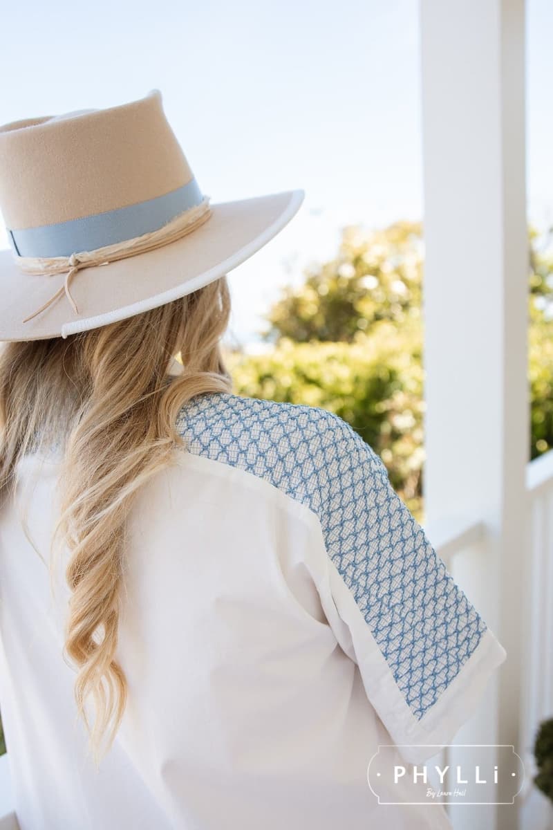 Back view of female model wearing the beige felt hat Kingston by PHYLLi Designs with Cornflower Japanese grosgrain bow band and ivory sari silk trim on a sunlit veranda.