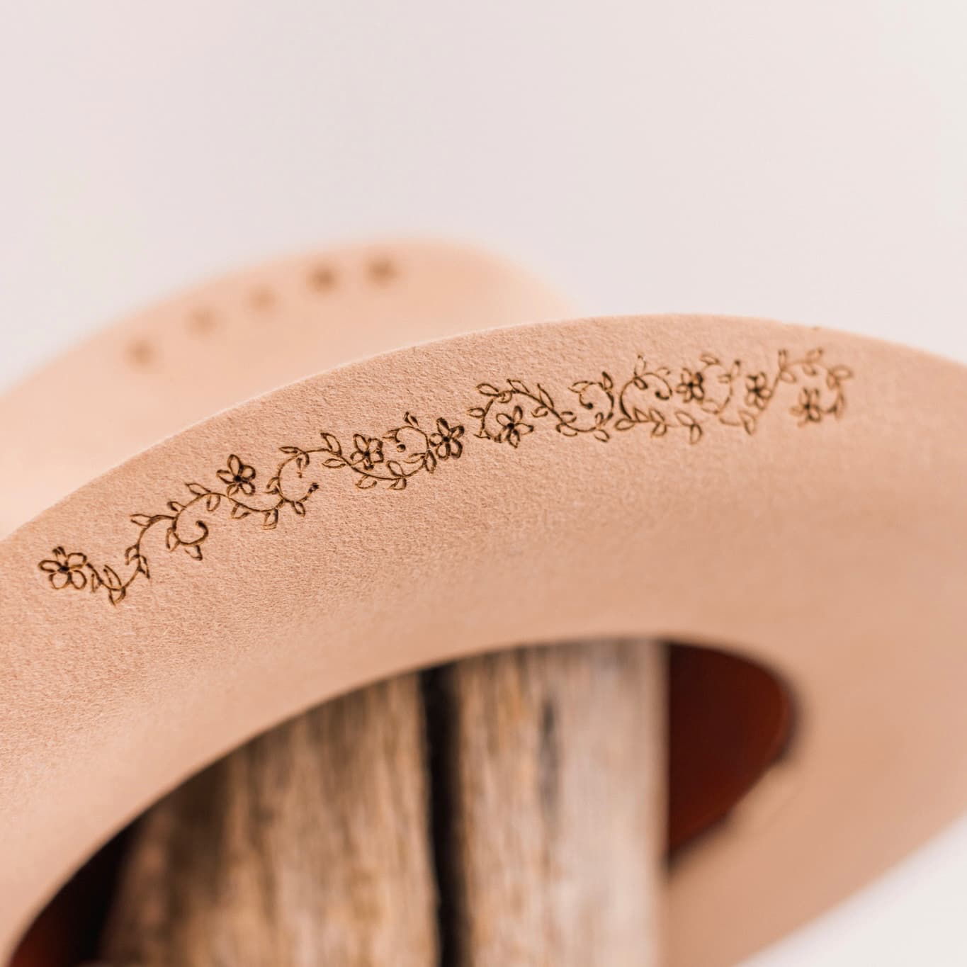 Close up detail of the La Fleurs camel felt cowboy hat by PHYLLi Designs showing delicate burnt branded botanical motif on the brim.