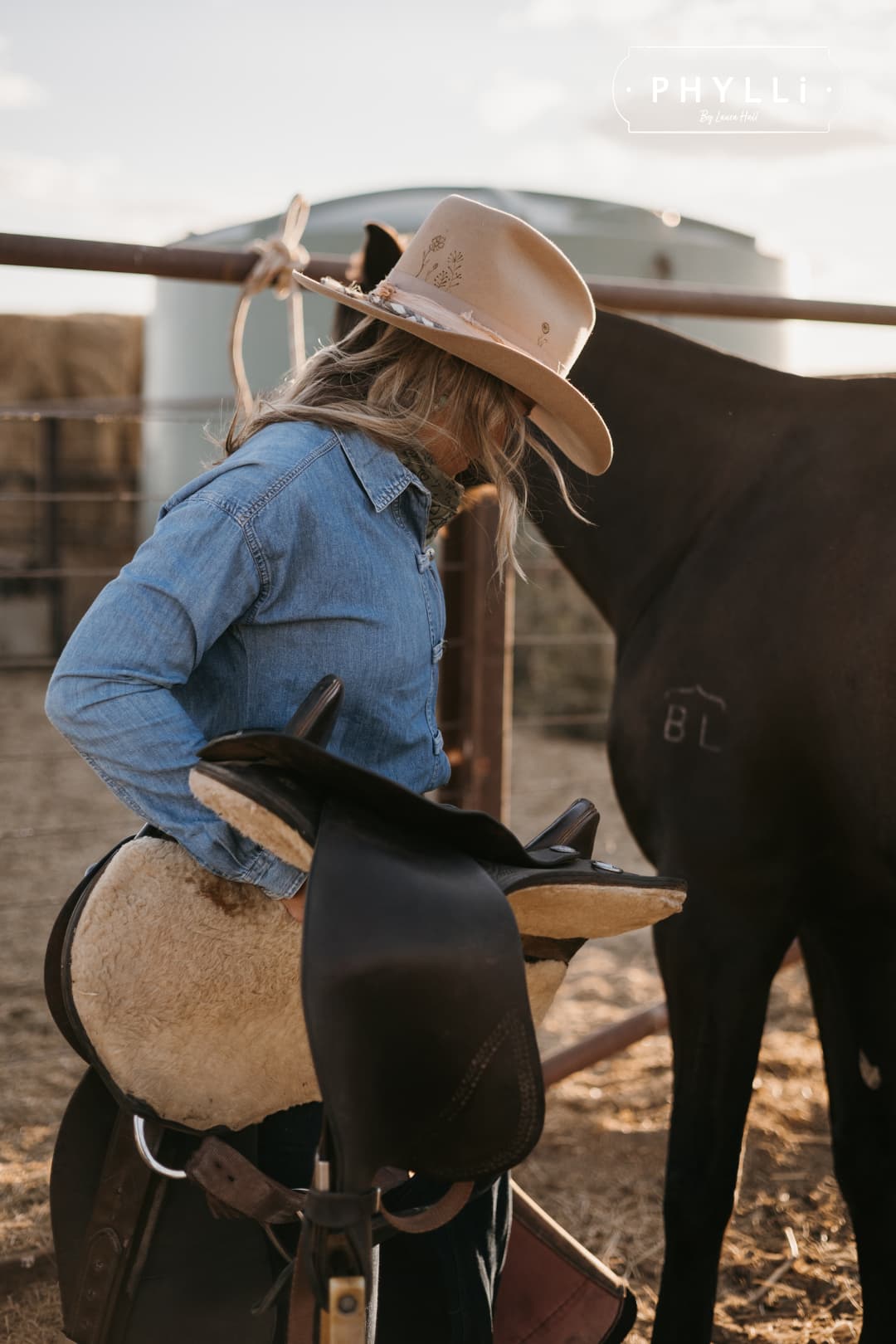 Cowgirl wearing the camel felt cowboy hat La Fleurs by PHYLLi Designs with braided sari silk trim while saddling a horse in an outback paddock.