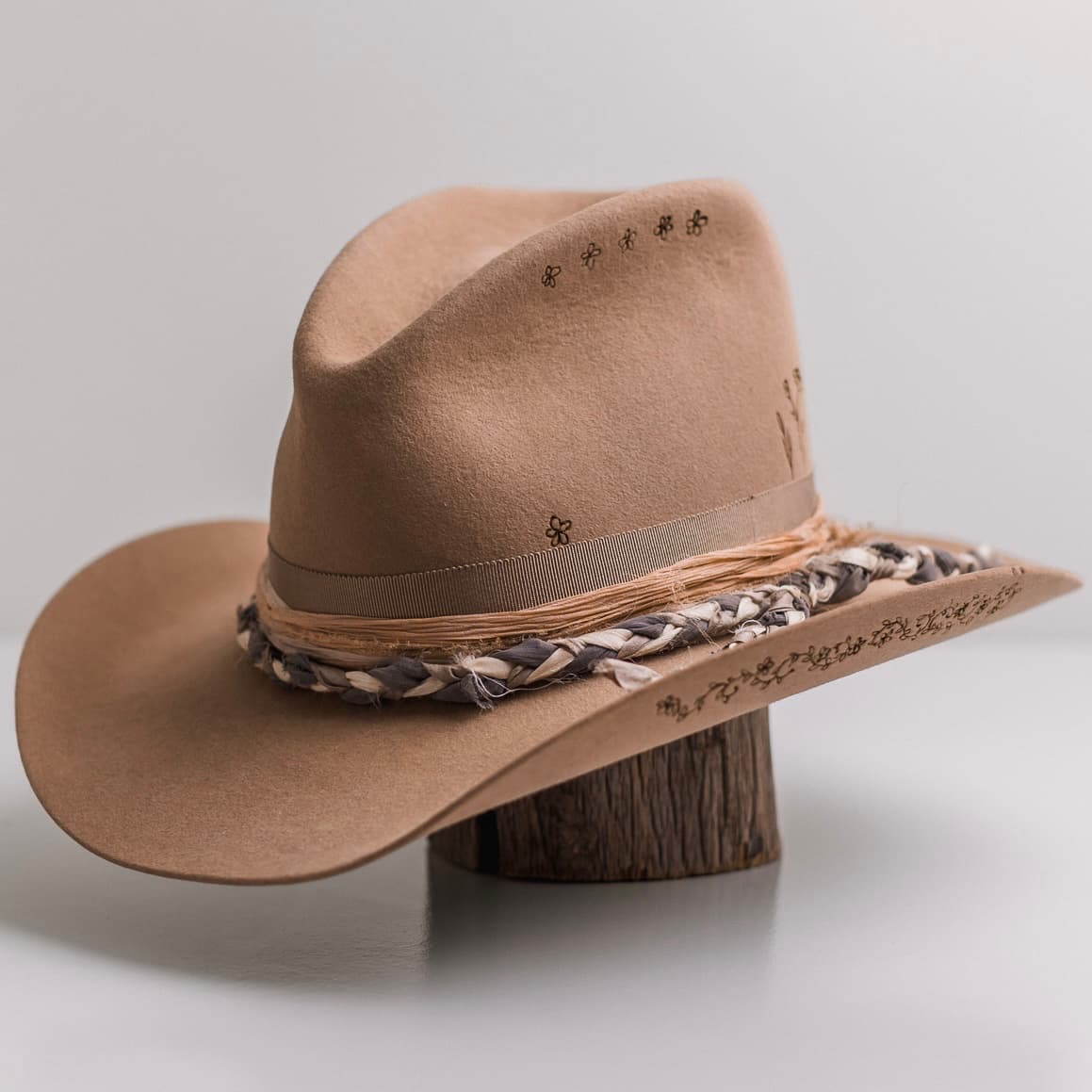 Front left angle of the camel felt cowboy hat La Fleurs by PHYLLi Designs with taupe grosgrain band braided sari silk trimming and floral branding.