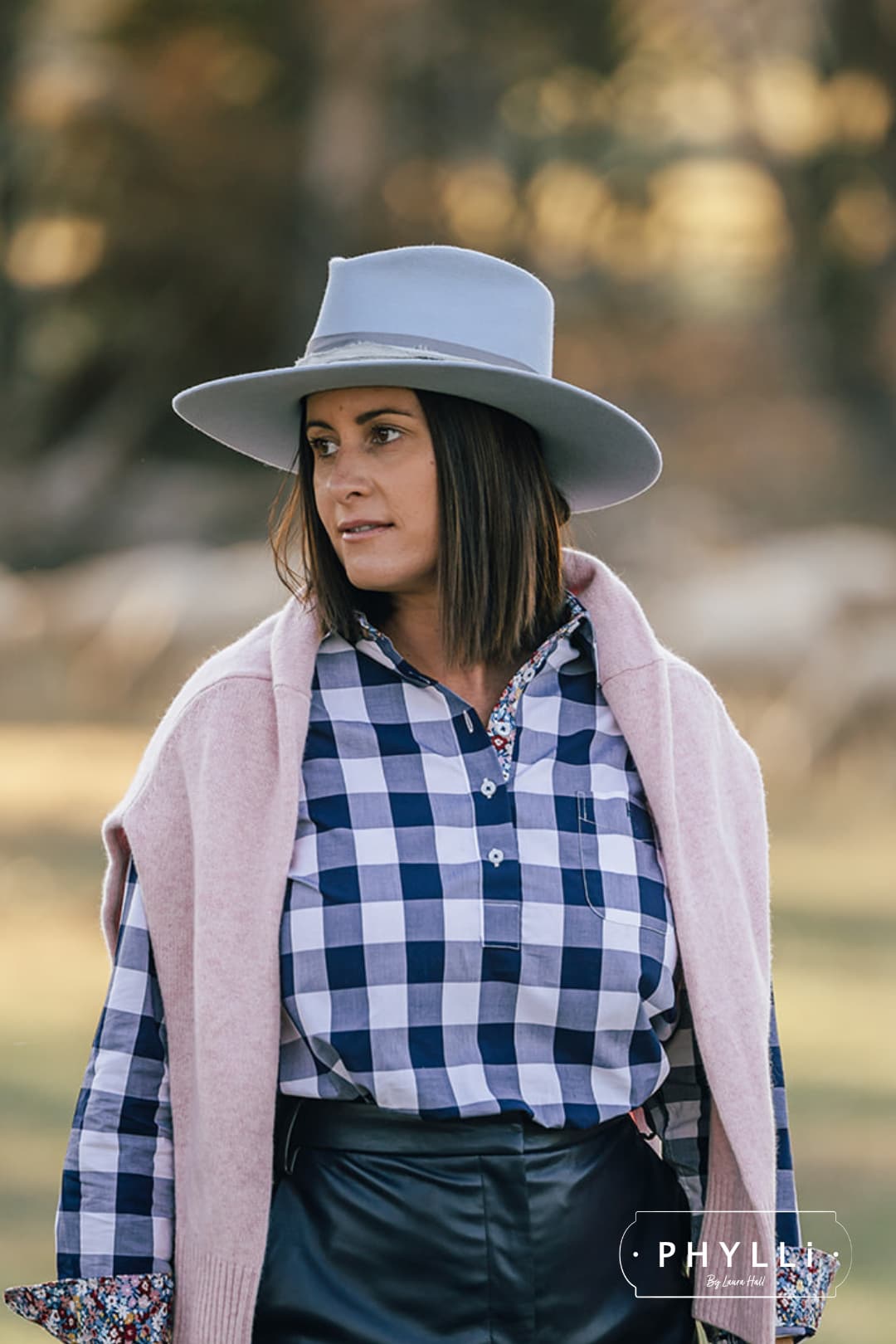 Woman wearing the La Journee Crystal Blue felt hat by PHYLLi Designs with cement grosgrain band in an outdoor countryside setting.
