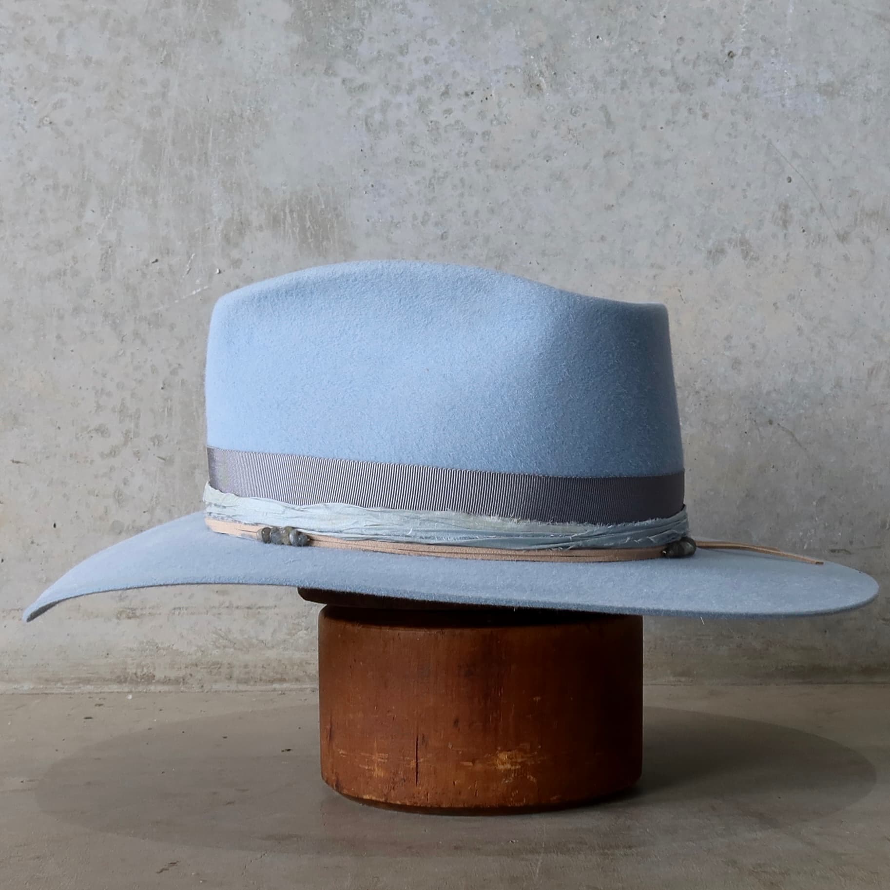 Left side view of the La Journee Crystal Blue felt hat by PHYLLi Designs with nude suede string and smokey quartz crystal cluster detail.