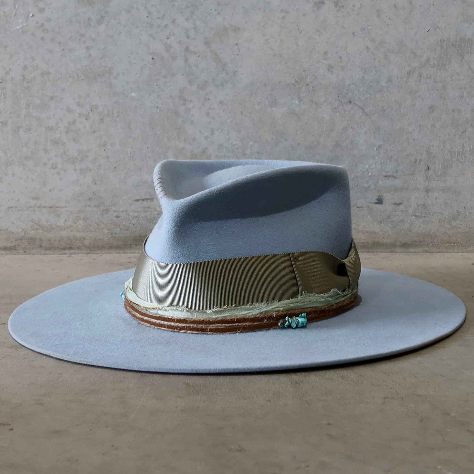 Front left angle of the crystal blue felt hat Lagoon by PHYLLi Designs with oil green grosgrain band, mint sari silk trim and turquoise crystal clusters.