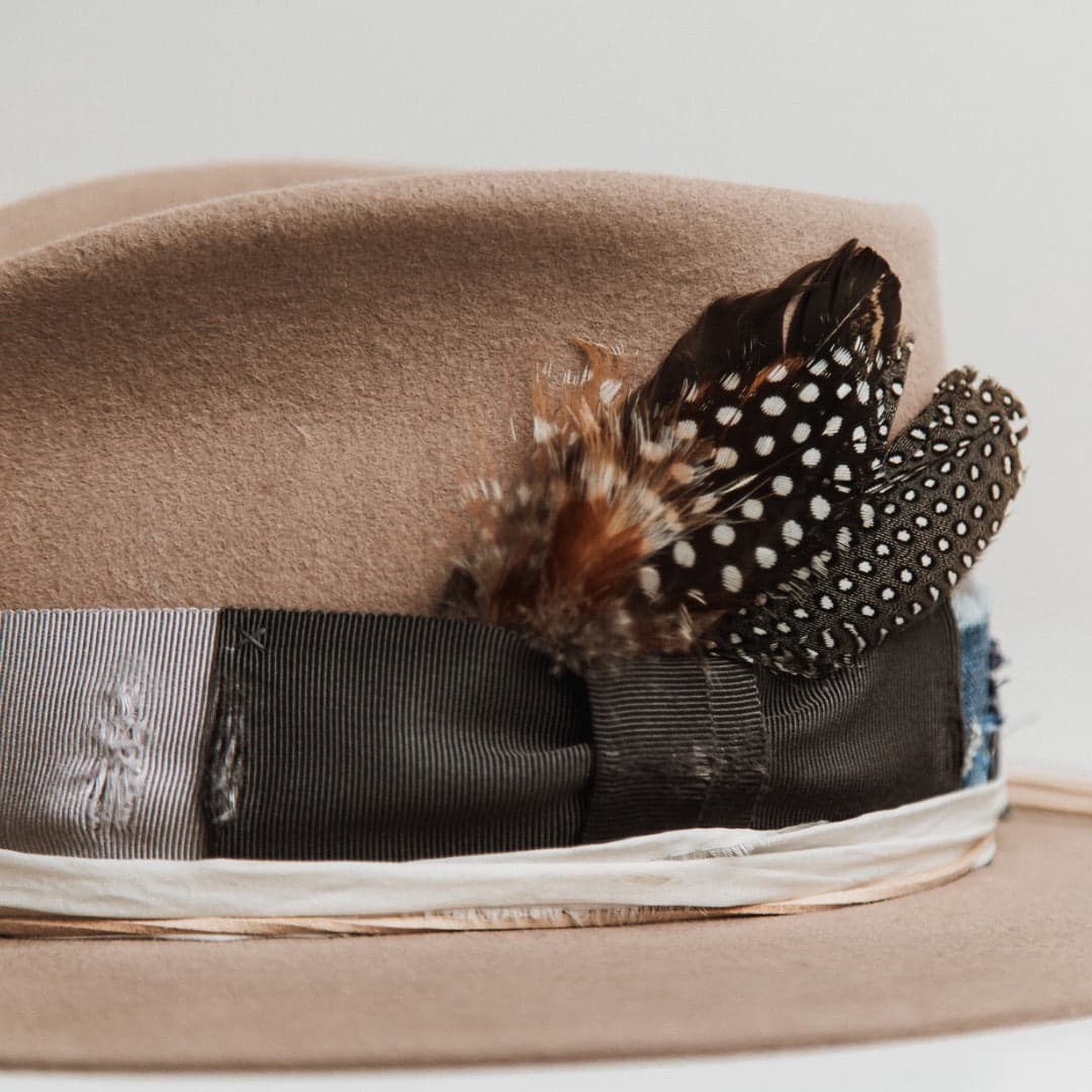 Close up detail of the Levi Limited Edition Sahara felt hat by PHYLLi Designs showing feather bunch, distressed grosgrain bow band and ivory sari silk trimming.
