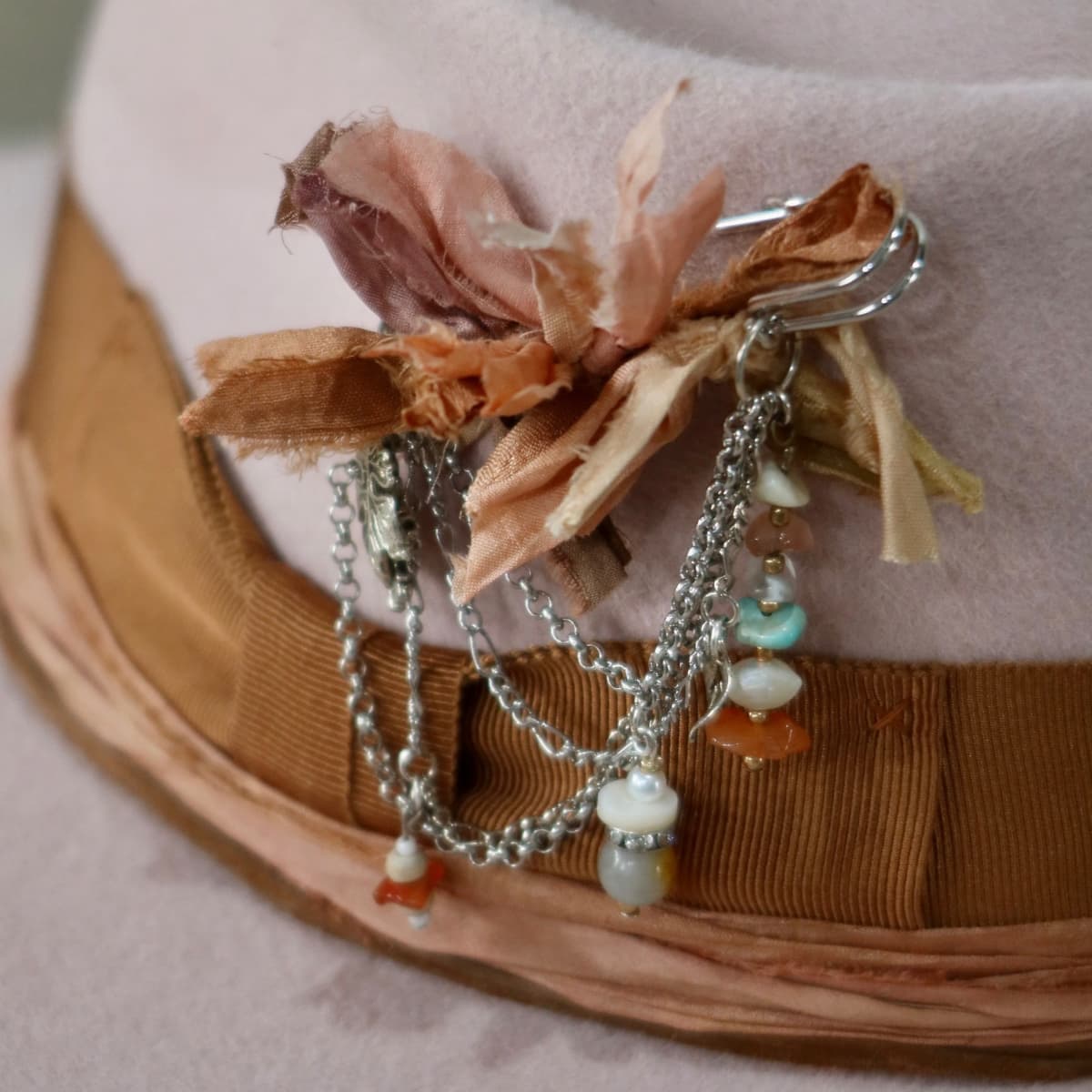 Close up detail of the Lexie felt hat showing silver chunky hat pin with sari silk ties, chains and beads.