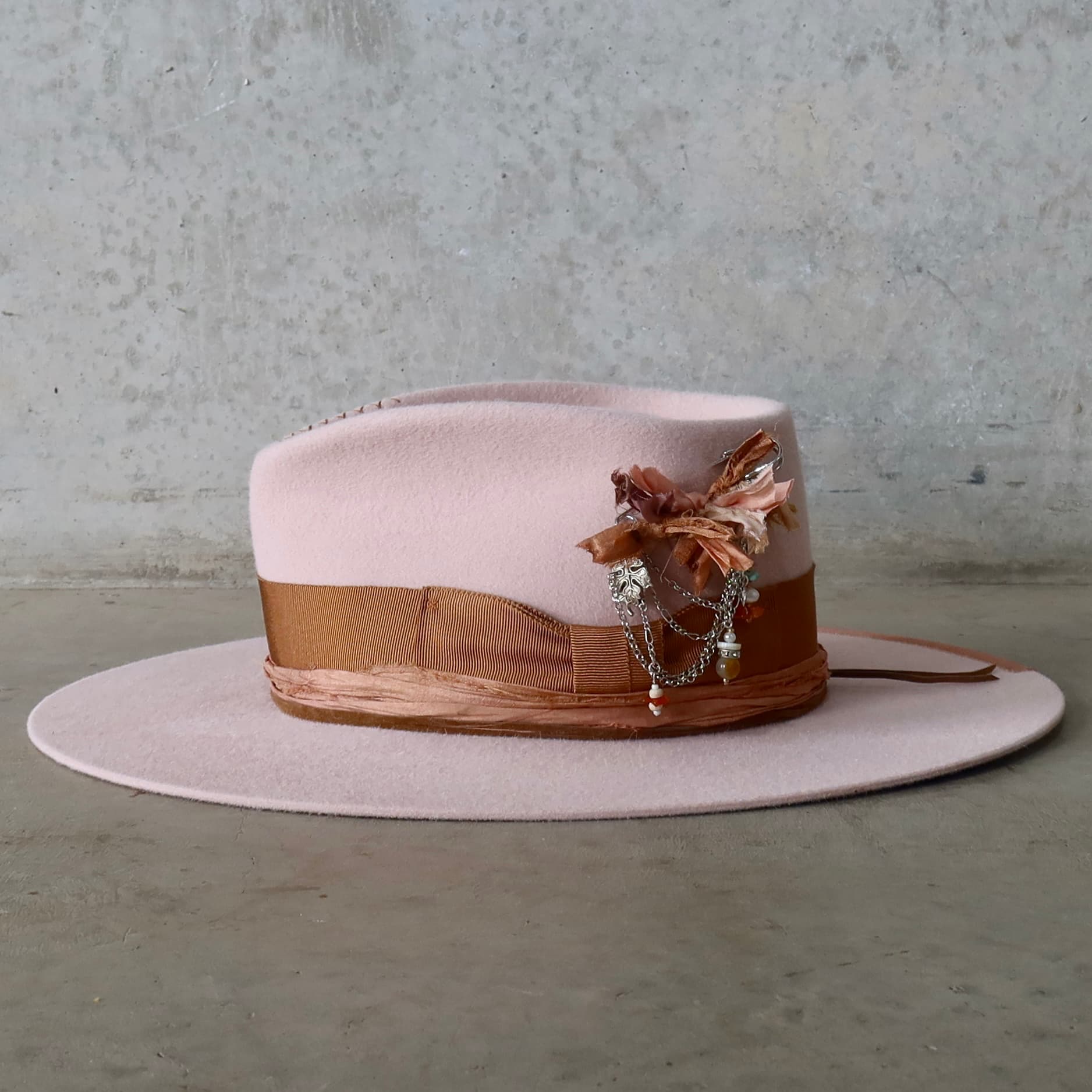 Left side view of the baby pink felt hat Lexie by PHYLLi Designs with silver chunky hat pin featuring sari silks, charms and beads.