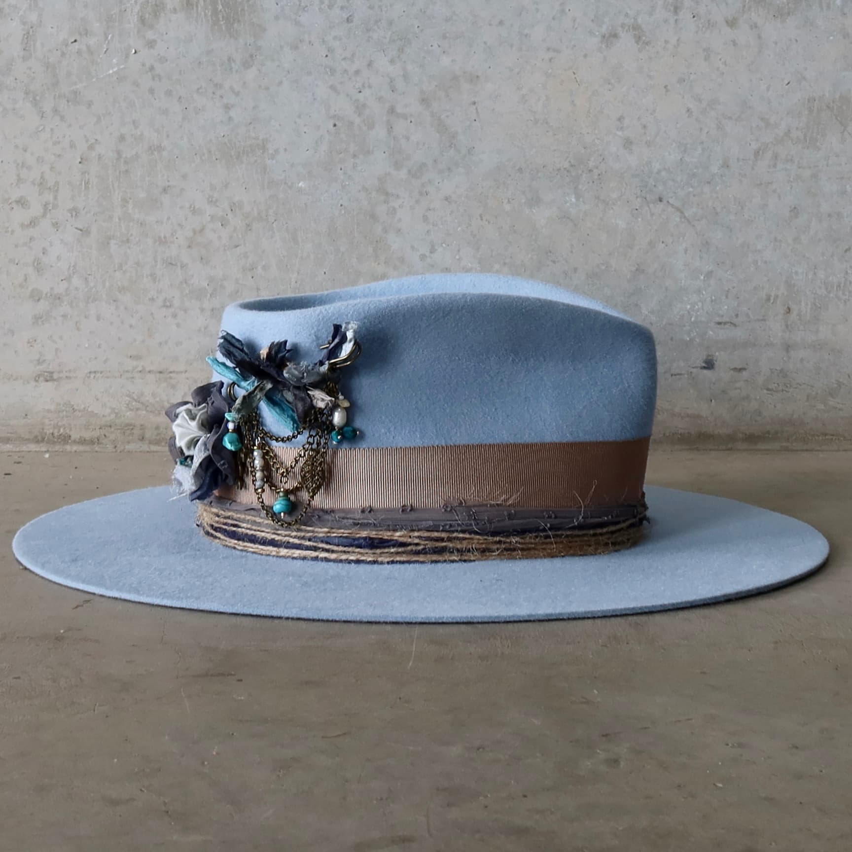 Right side view of the crystal blue felt hat Louise by PHYLLi Designs with removable sari silk Lapel Blooms and bronze chunky hat pin with charms and beads.