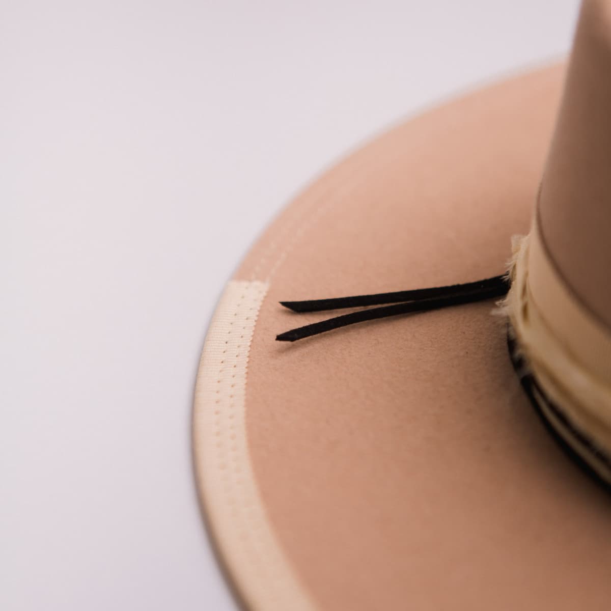 Close up detail of the Lover felt hat showing black suede string detail and sand double brim stitch.