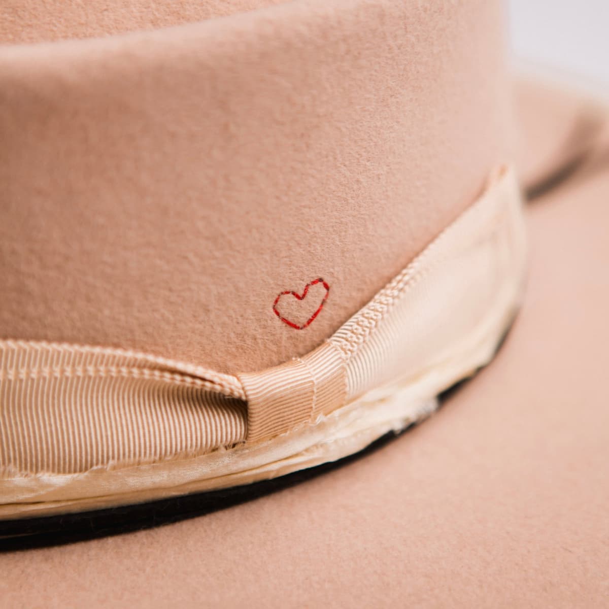 Close up detail of the Lover felt hat showing hand-stitched crimson heart on the crown beside the sand grosgrain band.