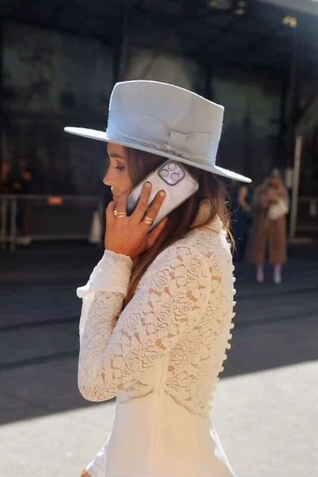 Model wearing the Crystal Blue felt hat Lucinda by PHYLLi Designs with cornflower grosgrain bow band while standing outdoors in an urban setting.