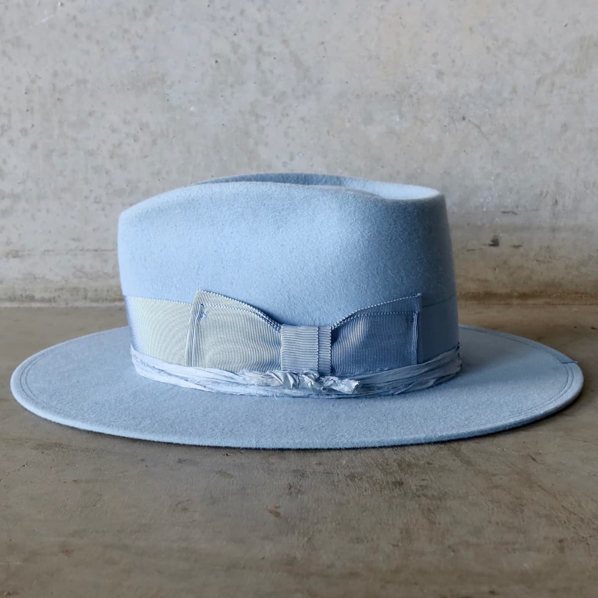 Left side view of the Crystal Blue felt hat Lucinda by PHYLLi Designs with cornflower grosgrain brim trim and tonal blue sari silk trimming.