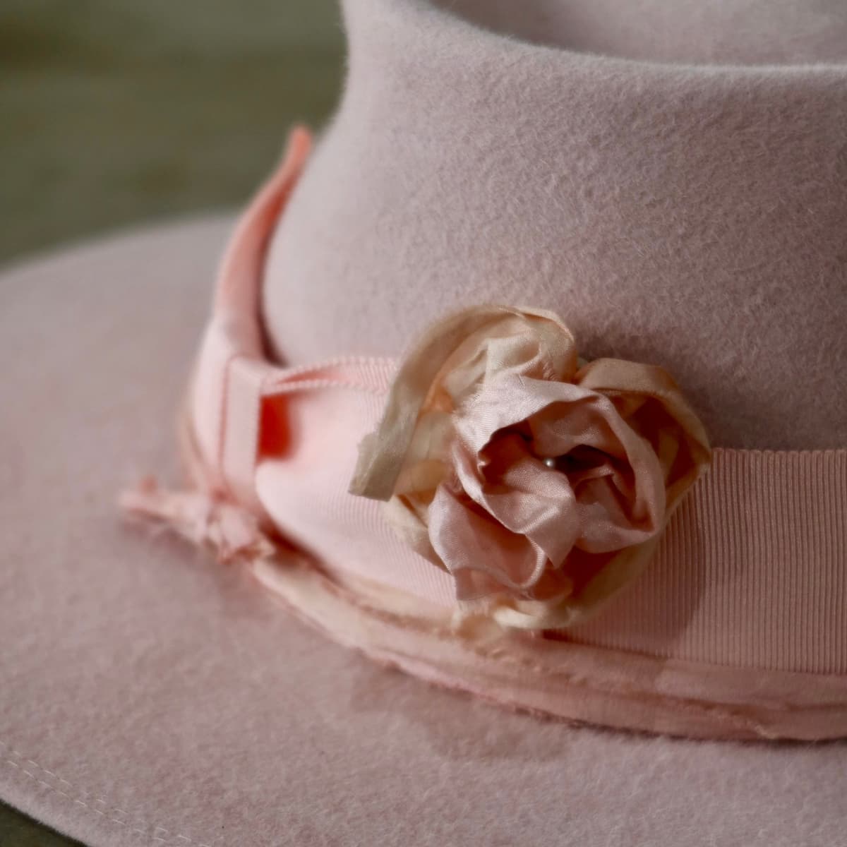 Close up detail of the Lucinda Bloom felt hat showing removable tonal pink sari silk lapel bloom with pearl centre attached to the salmon grosgrain band.