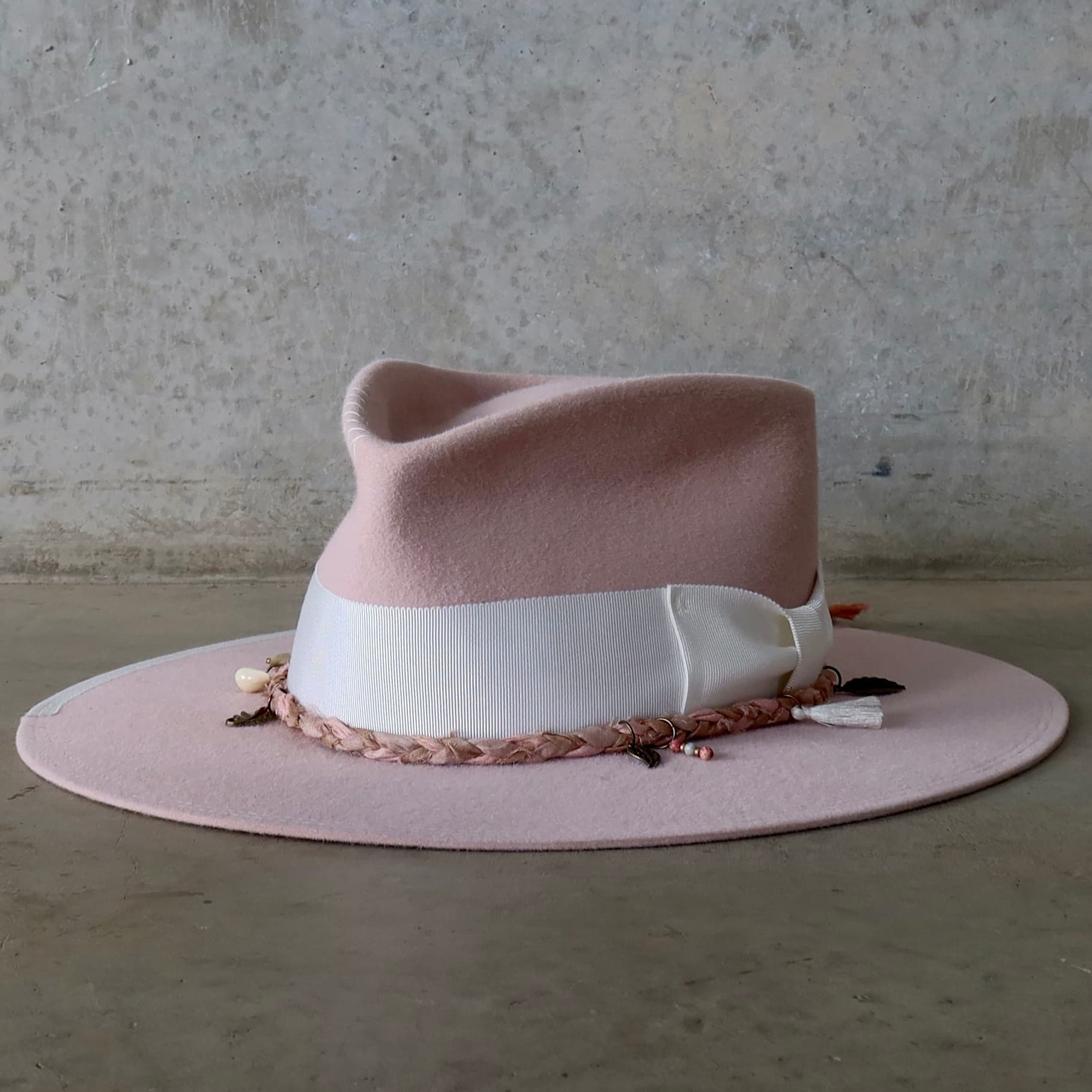 Front left angle of the baby pink felt hat Lucky Charm by PHYLLi Designs with ivory grosgrain bow band and Charm Plait in pink sari silks.