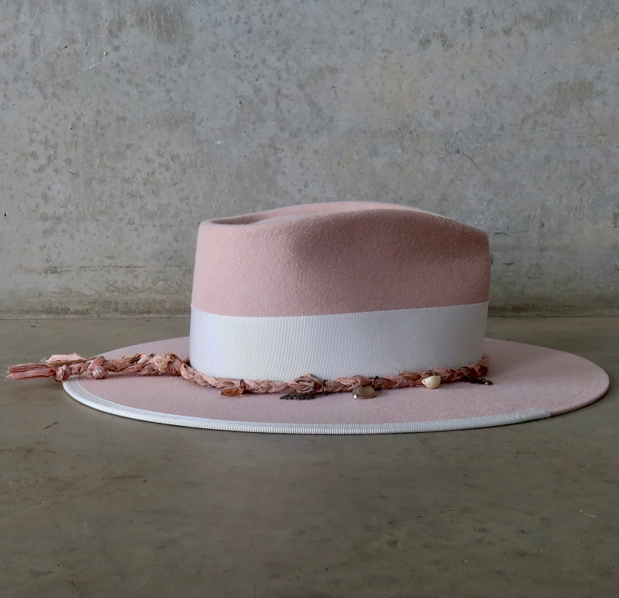 Right side view of the baby pink felt hat Lucky Charm by PHYLLi Designs with ivory Japanese grosgrain bow band and tonal pink Charm Plait featuring bronze charms, bead pendants and ivory tassel.