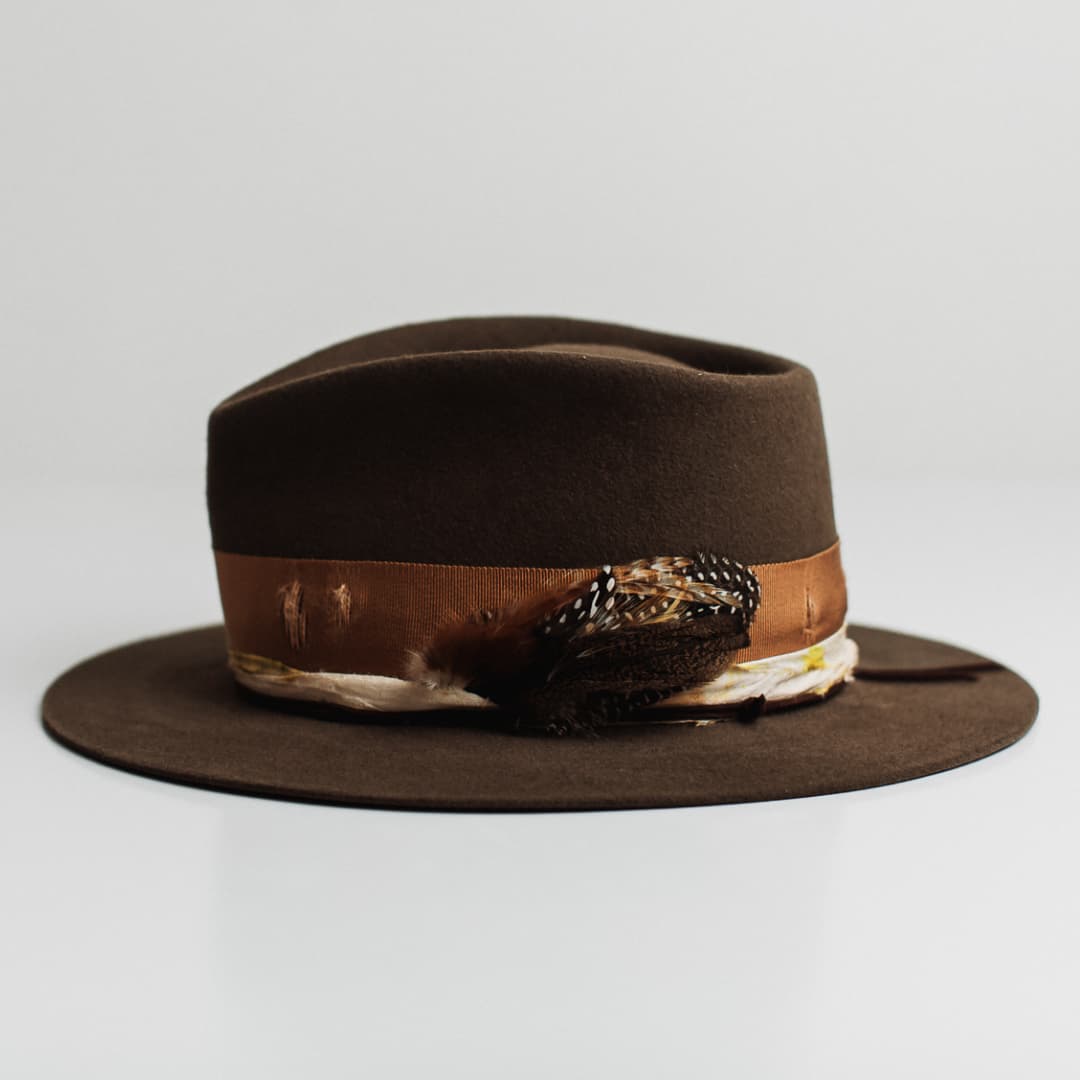 Left side view of the Lucky Findings dirty olive felt hat by PHYLLi Designs with chocolate suede string and assorted fallen feather bunch.