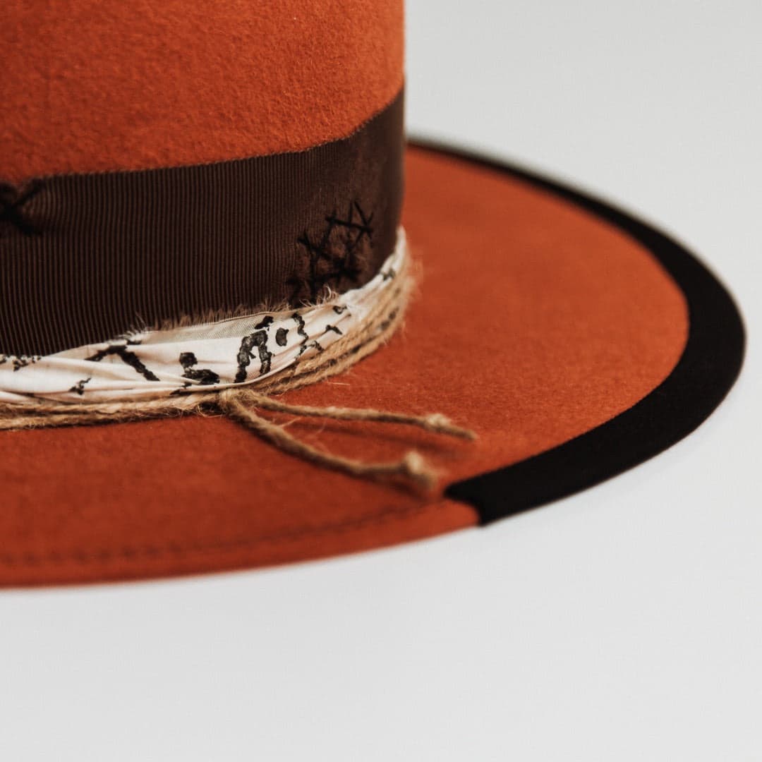 Close up detail of the Marrakech spiced pumpkin felt hat by PHYLLi Designs showing black grosgrain brim trim with twine wraps and black and white sari silk trimming.