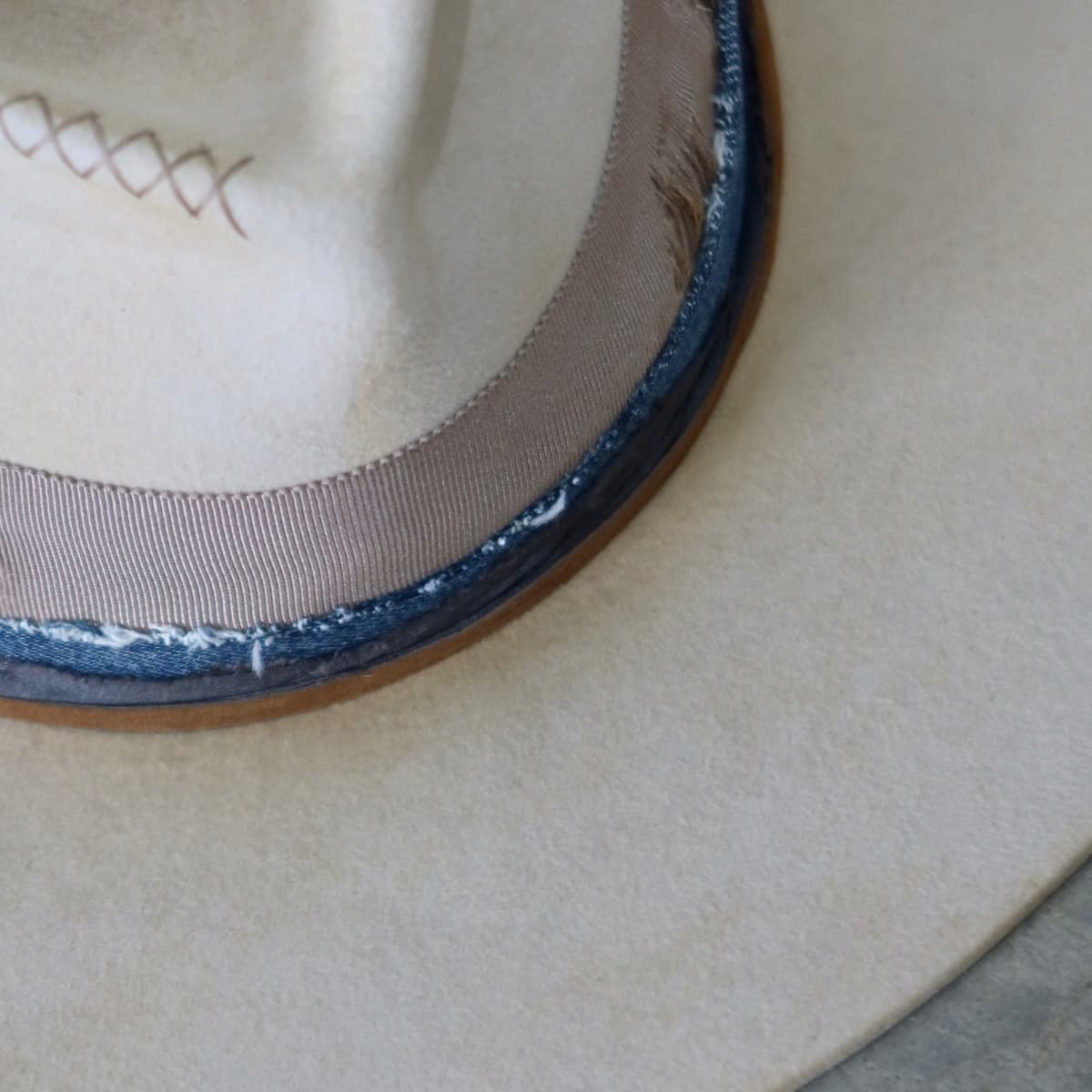 Close up detail of the McVeigh felt hat showing distressed beige felt with taupe grosgrain band and layered navy sari silk and denim trimming along the crown.