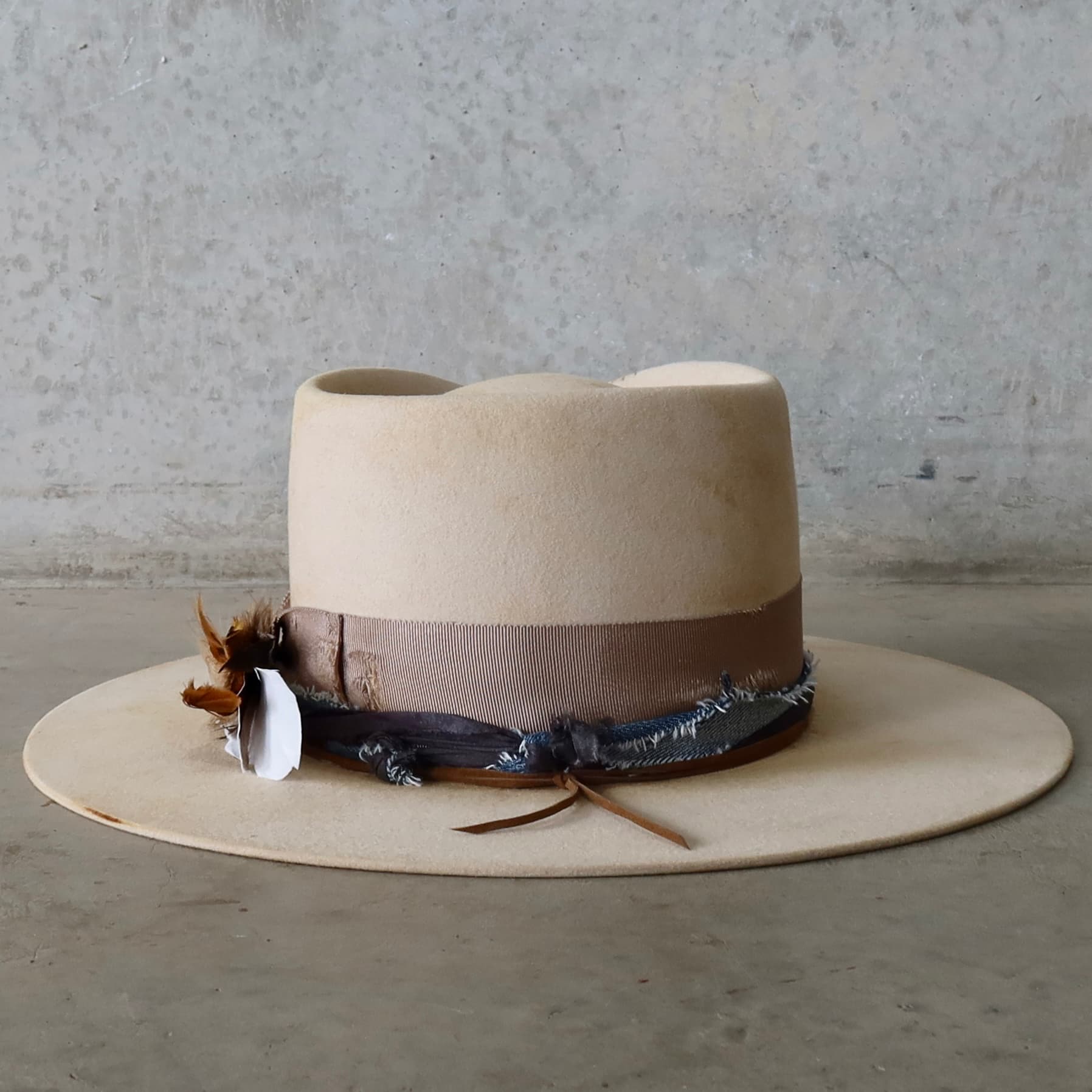 Back view of the beige distressed felt hat McVeigh by PHYLLi Designs featuring navy sari silk and denim trim tied with tan suede string.