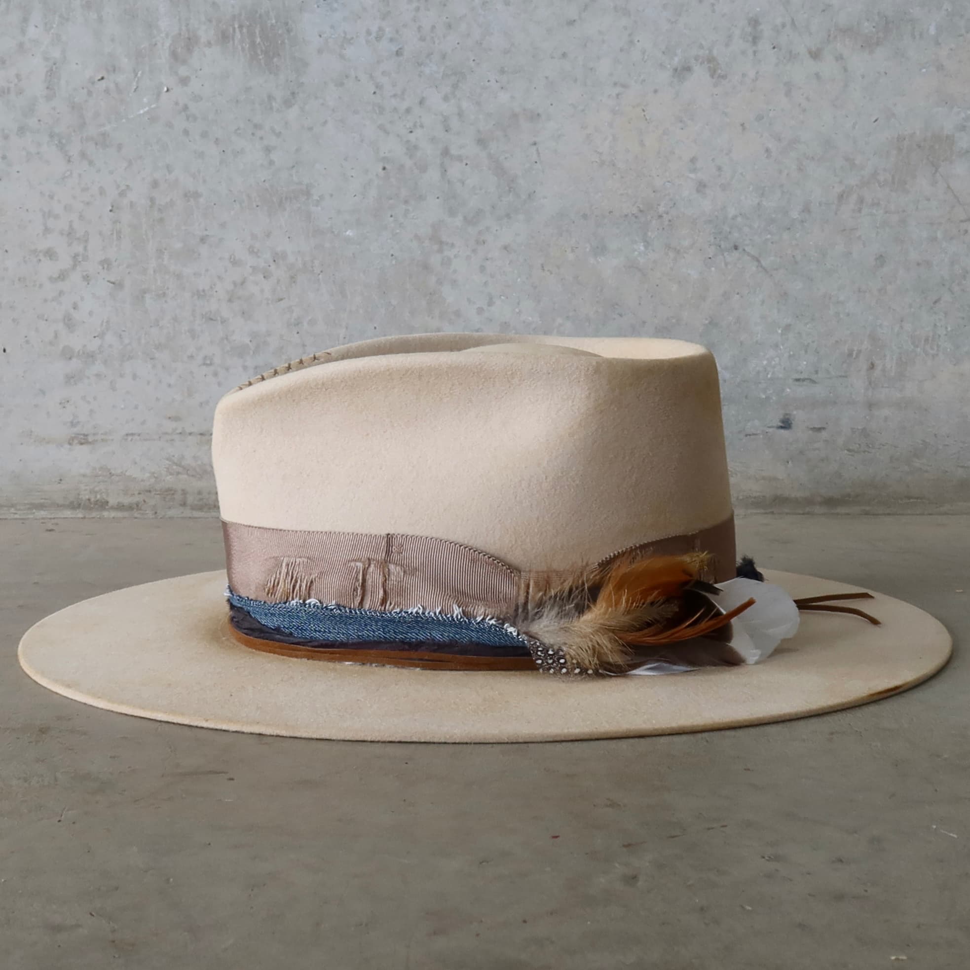Left side view of the beige distressed felt hat McVeigh by PHYLLi Designs with taupe distressed grosgrain band, navy sari silk and denim trimming.