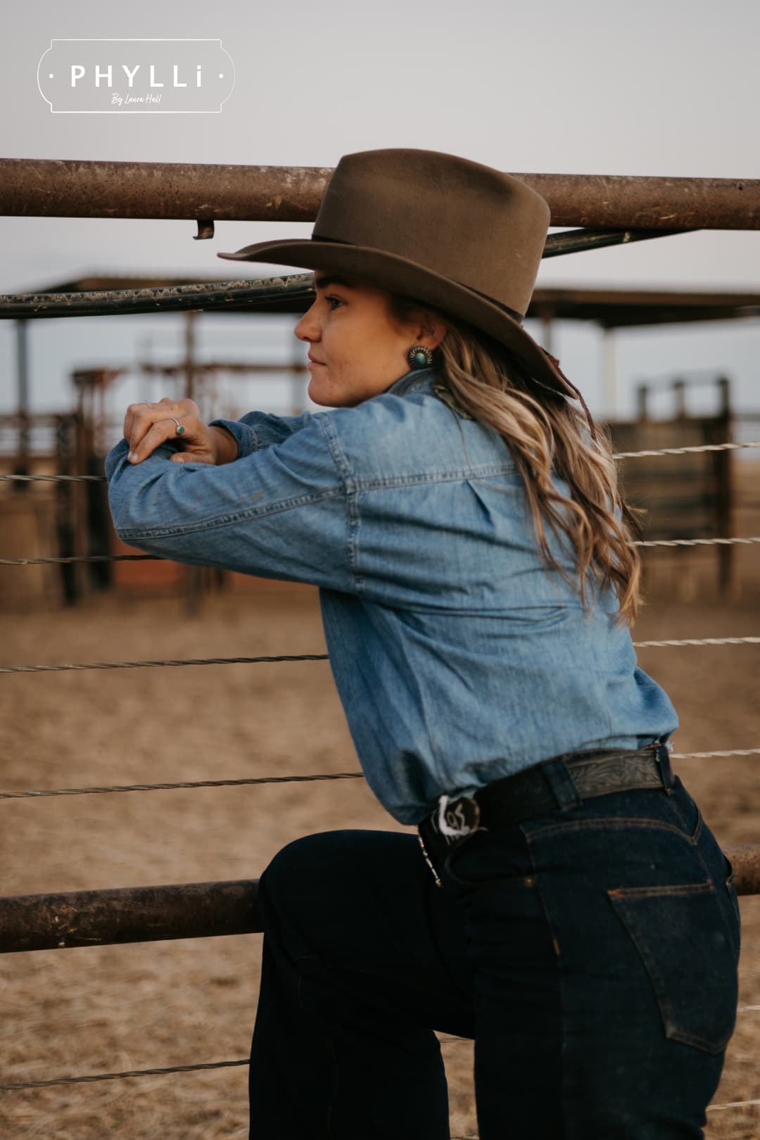 Woman wearing the Midnight Cowboy dirty olive felt cowboy hat by PHYLLi Designs in rural cattle yards.