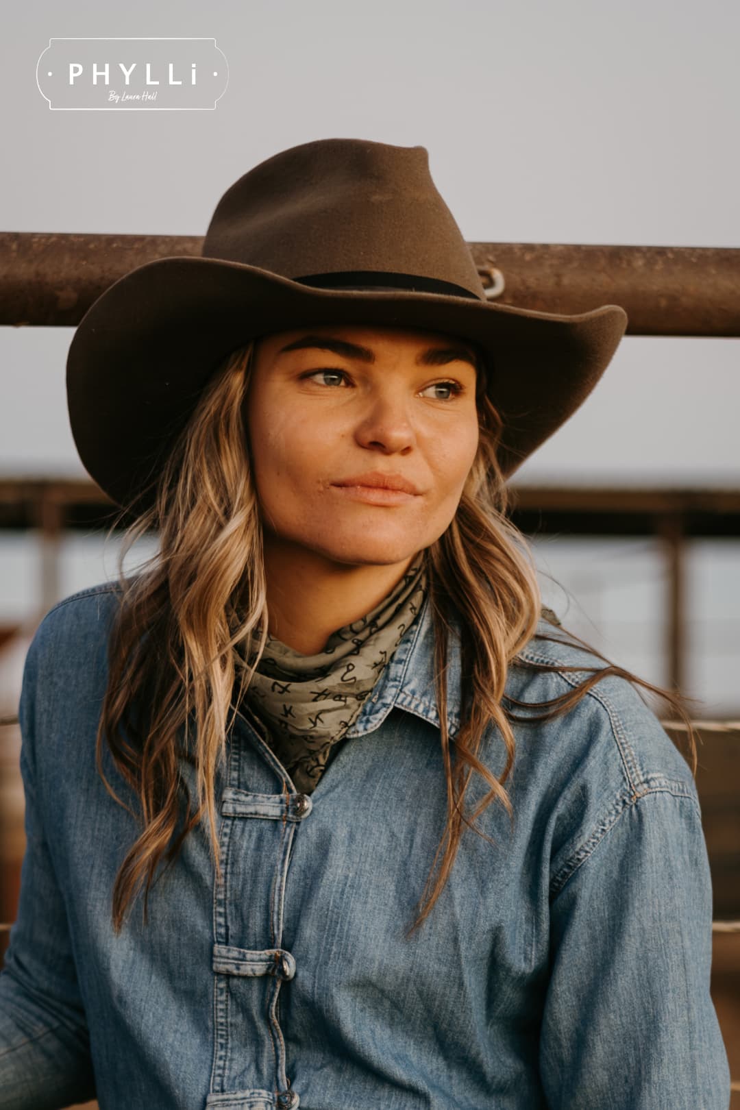 Close up woman wearing the Midnight Cowboy dirty olive felt cowboy hat by PHYLLi Designs with black Japanese grosgrain ribbon band and midnight sari silk trim in cattle yards.