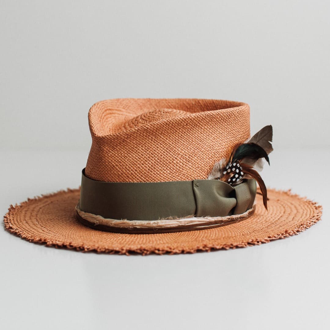 Front left angle of the Nim Panama biscuit Panama hat by PHYLLi Designs with oil green grosgrain band and fallen feather bunch.
