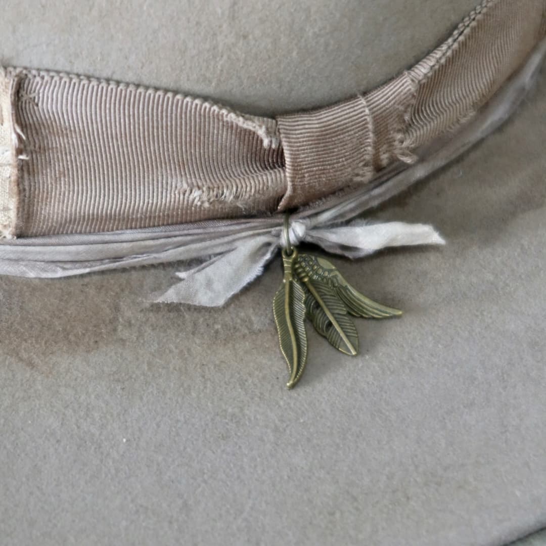 Close up detail of the Oakley Limited Edition felt hat showing bronze feather charm cluster on sari silk trim.