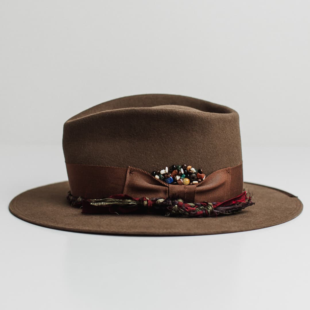 Left side view of the Olive Enchanted dirty olive felt hat by PHYLLi Designs with chocolate grosgrain band and plaited sari silk trimming.