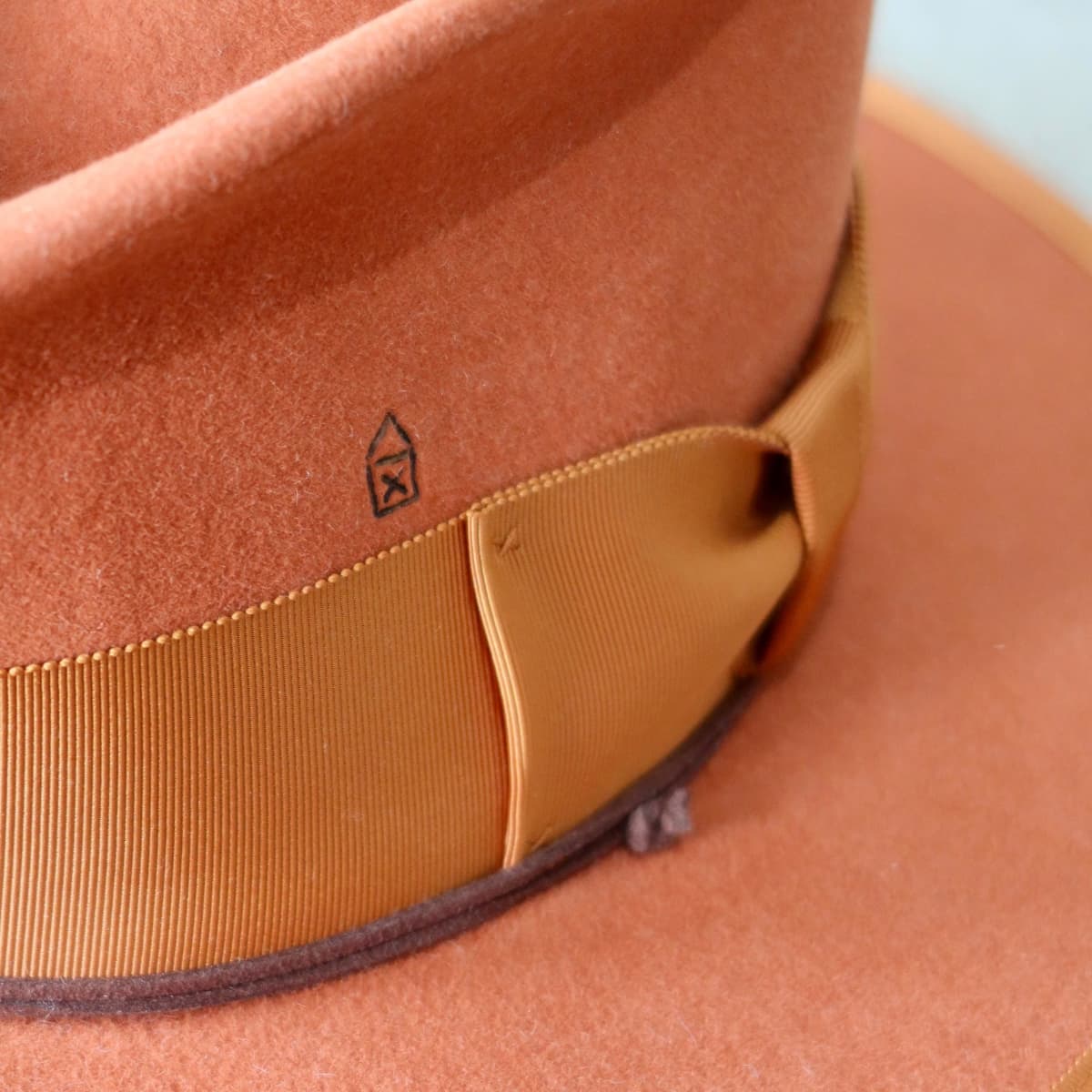 Close up detail of the Patrick felt hat showing rust Japanese grosgrain bow band and burnt branded symbol on crown.